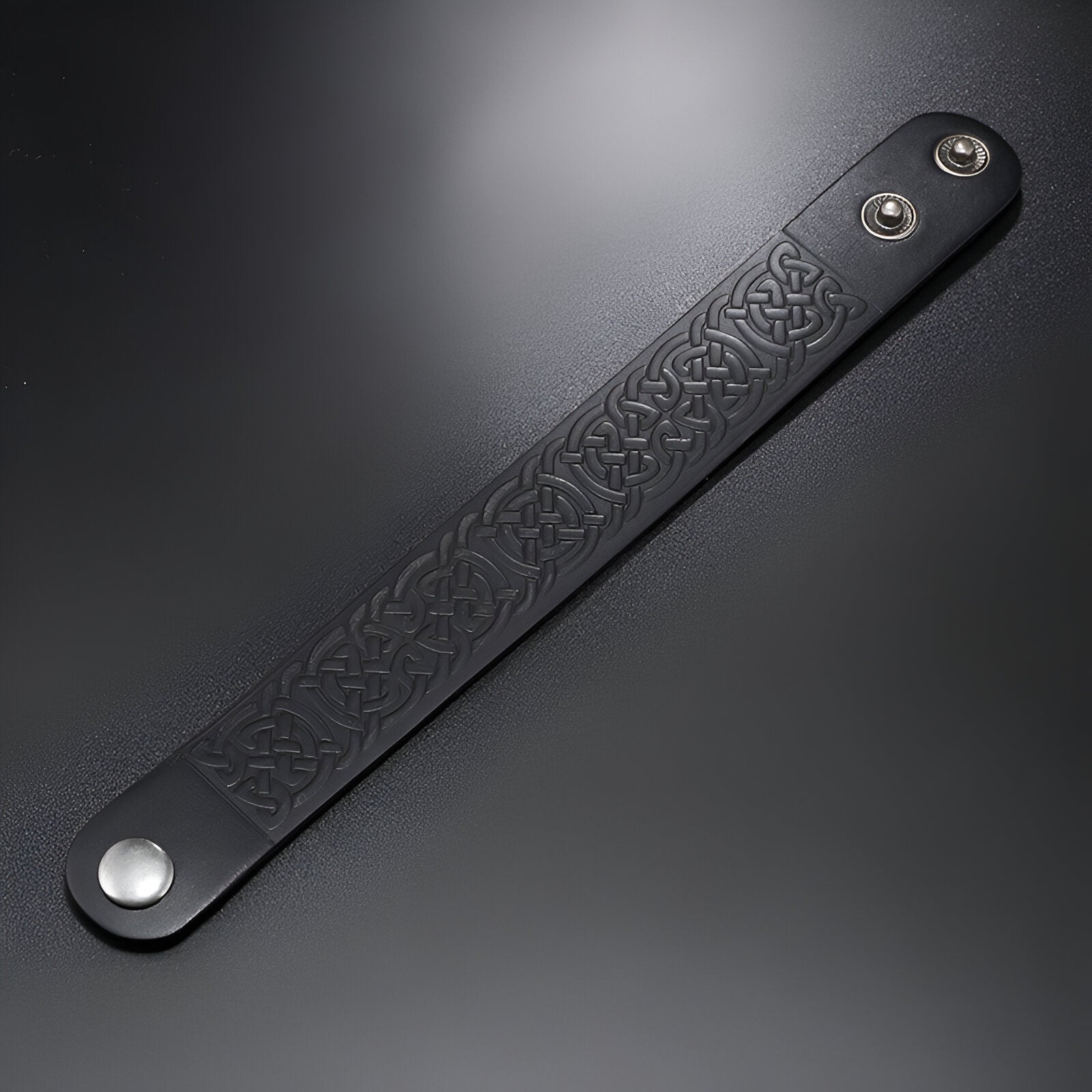 Bracelet en cuir noir pour homme avec motifs gaufrés et fermoir à pression métallique argenté.