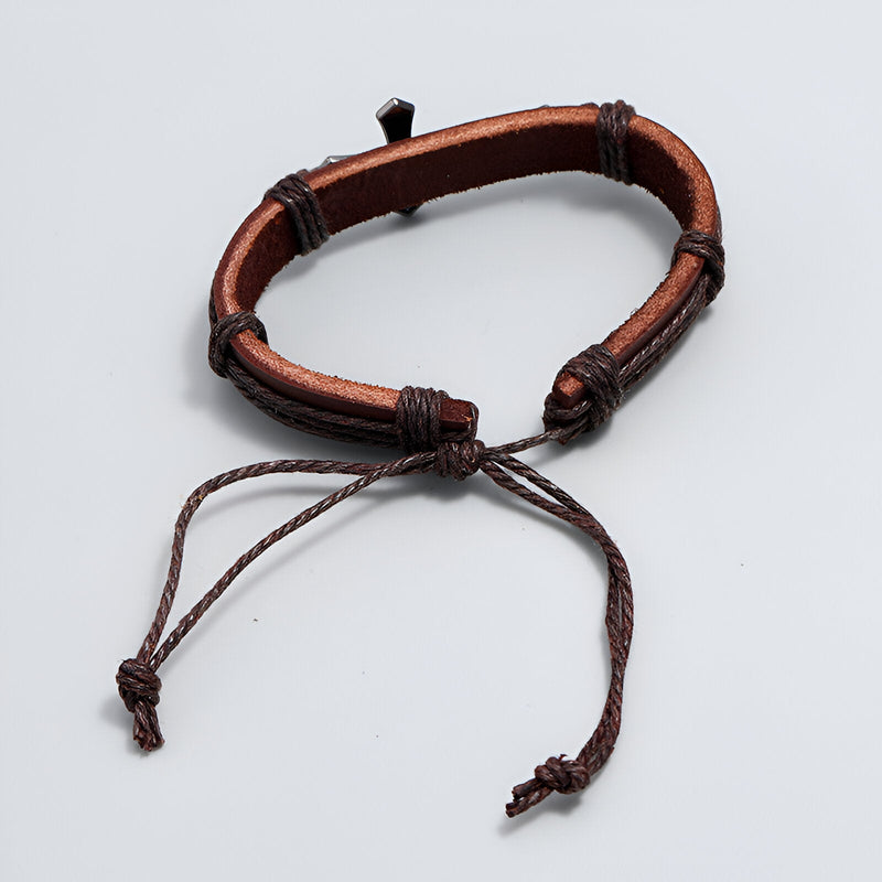 Bracelet en cuir marron avec croix chrétienne en métal, ajustable par cordon tressé.