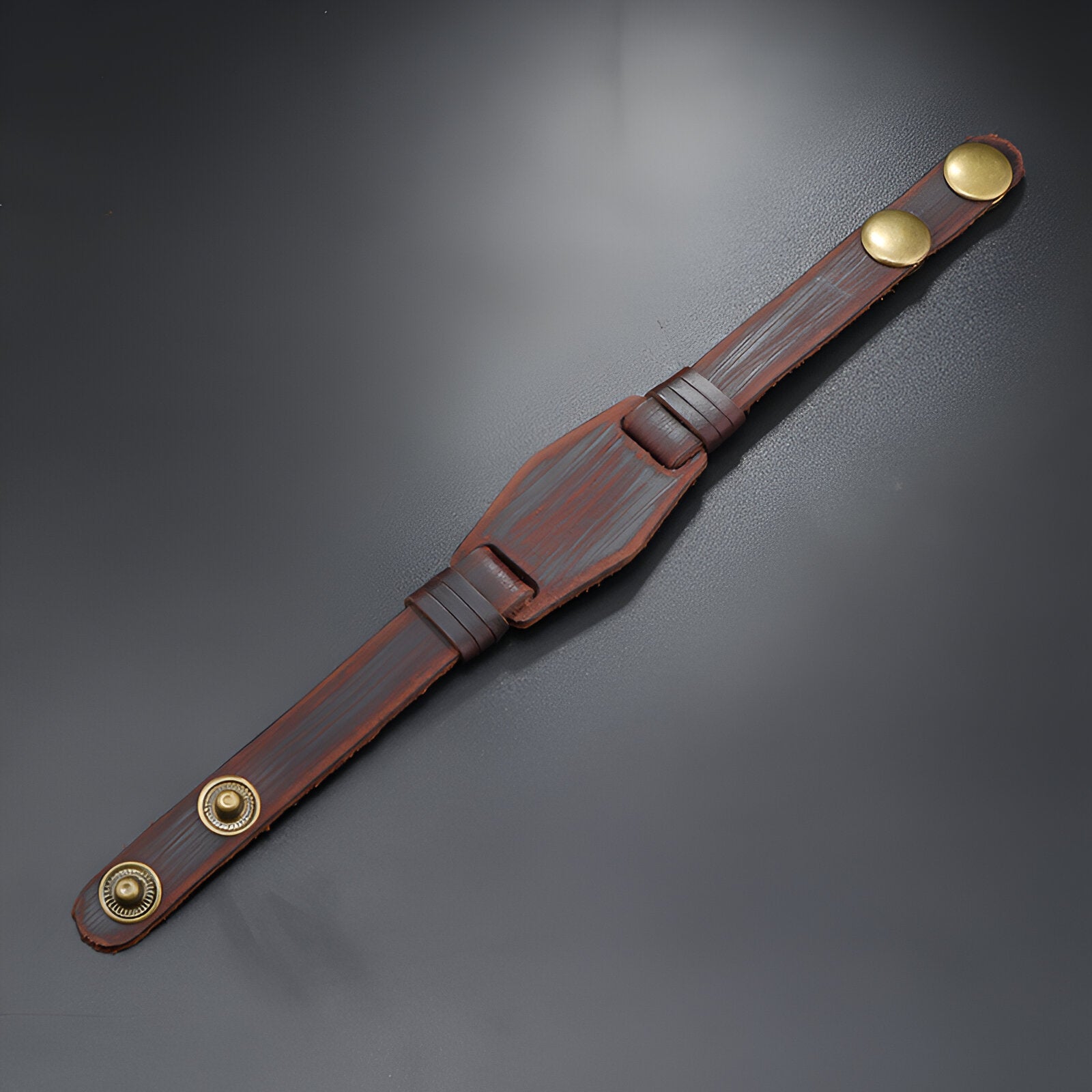Bracelet homme en cuir marron large avec double bouton-pression doré et surpiqûres rouges.