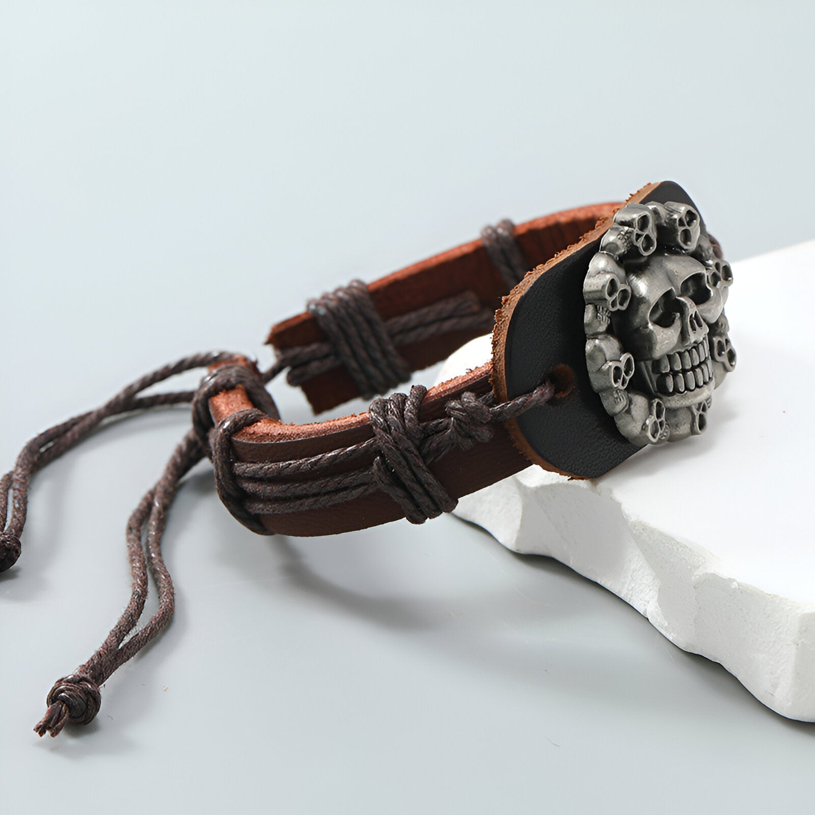 Bracelet en cuir marron avec pendentif tête de mort en métal gris et cordons réglables.