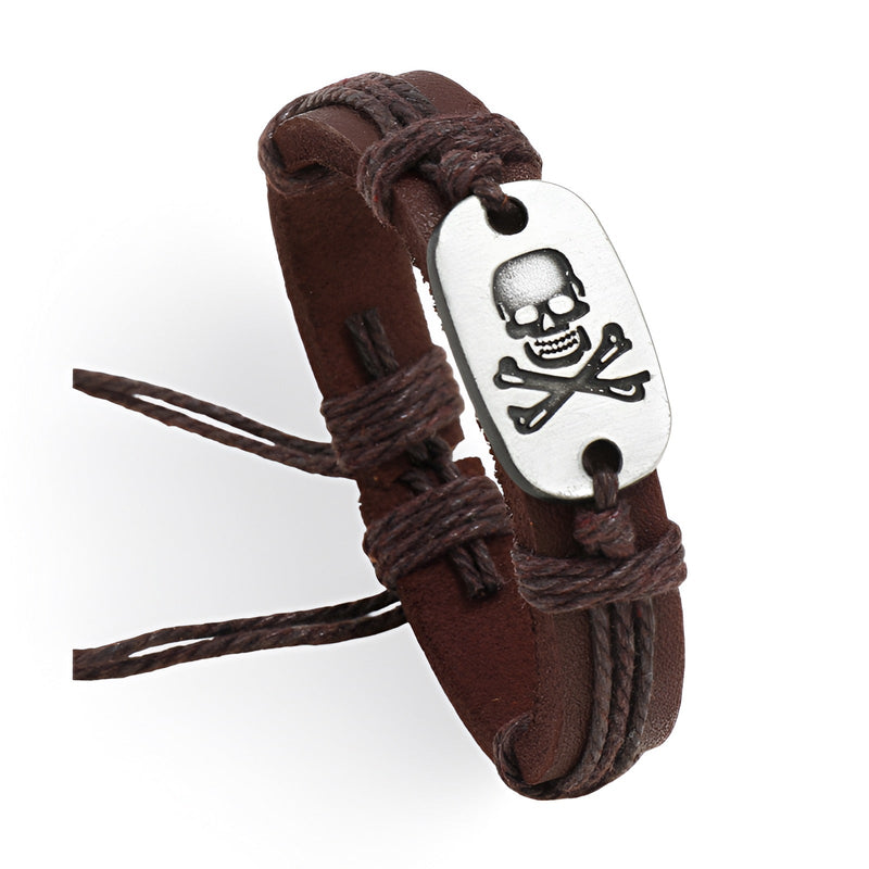Bracelet en cuir marron avec plaque métal argentée ornée d'une tête de mort et liens en cordettes brunes.