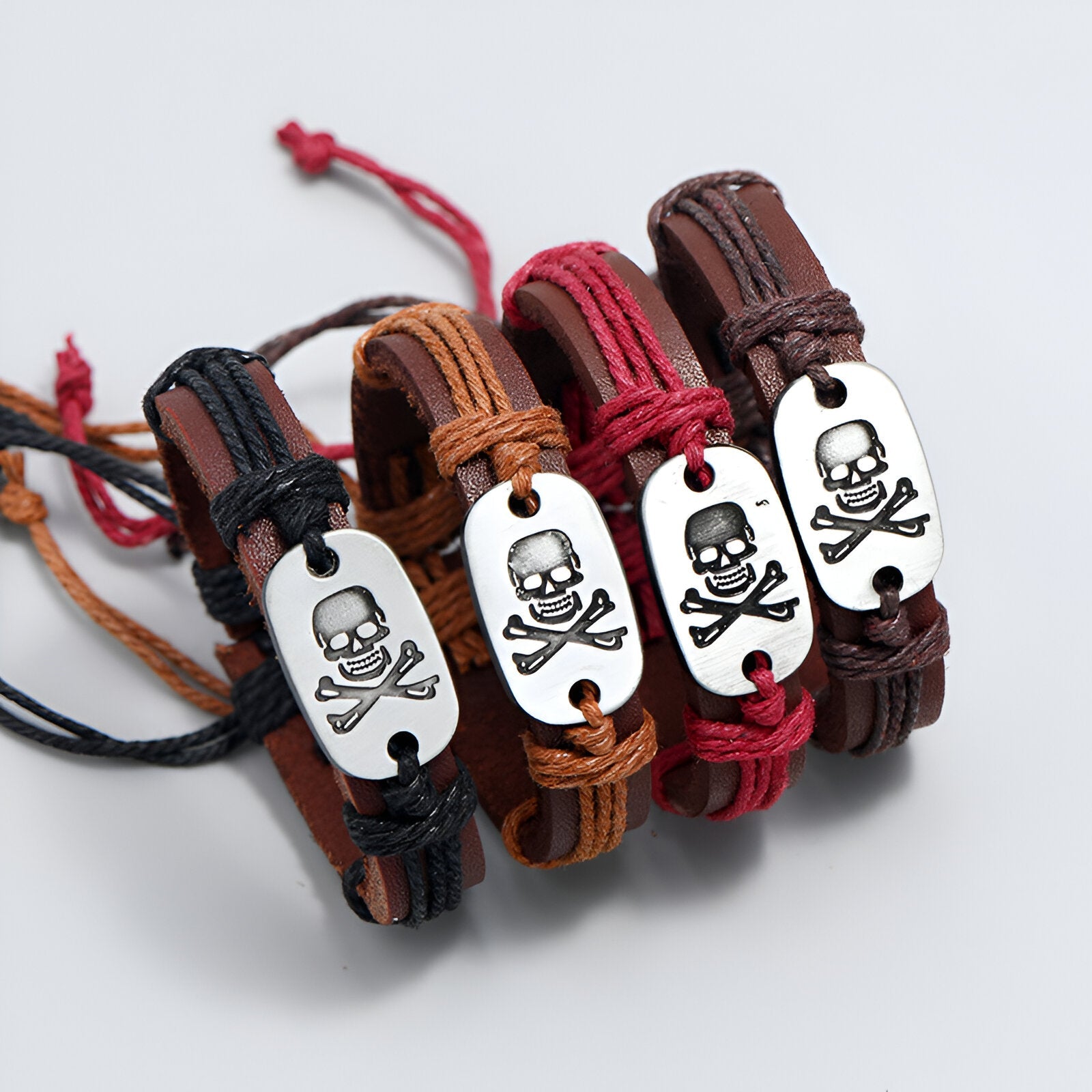 Bracelets en cuir tressé noir, marron clair, rouge et marron foncé avec plaque métal tête de mort gravée.