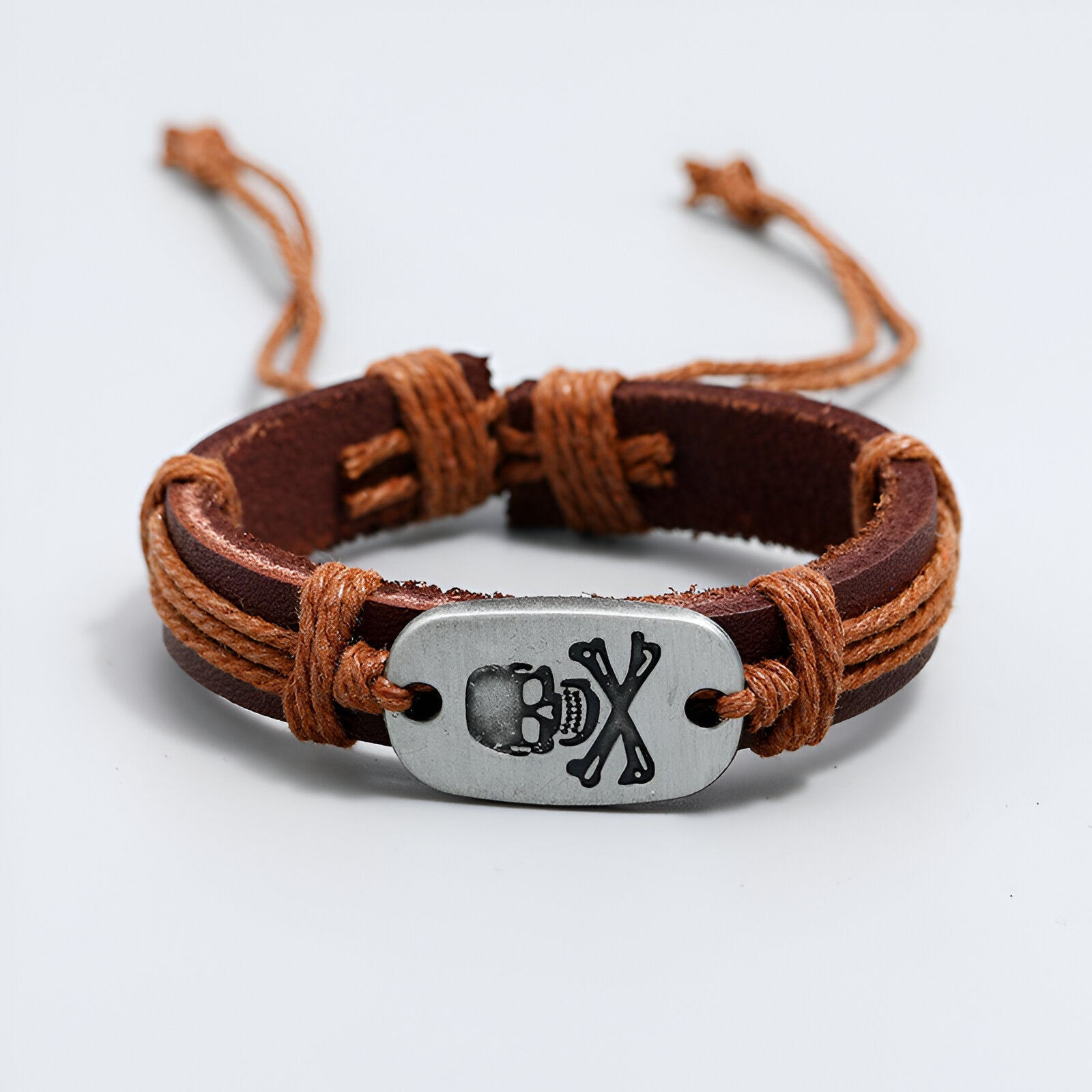 Bracelet en cuir marron avec lacets, plaque métal argentée gravée tête de mort et os croisés.