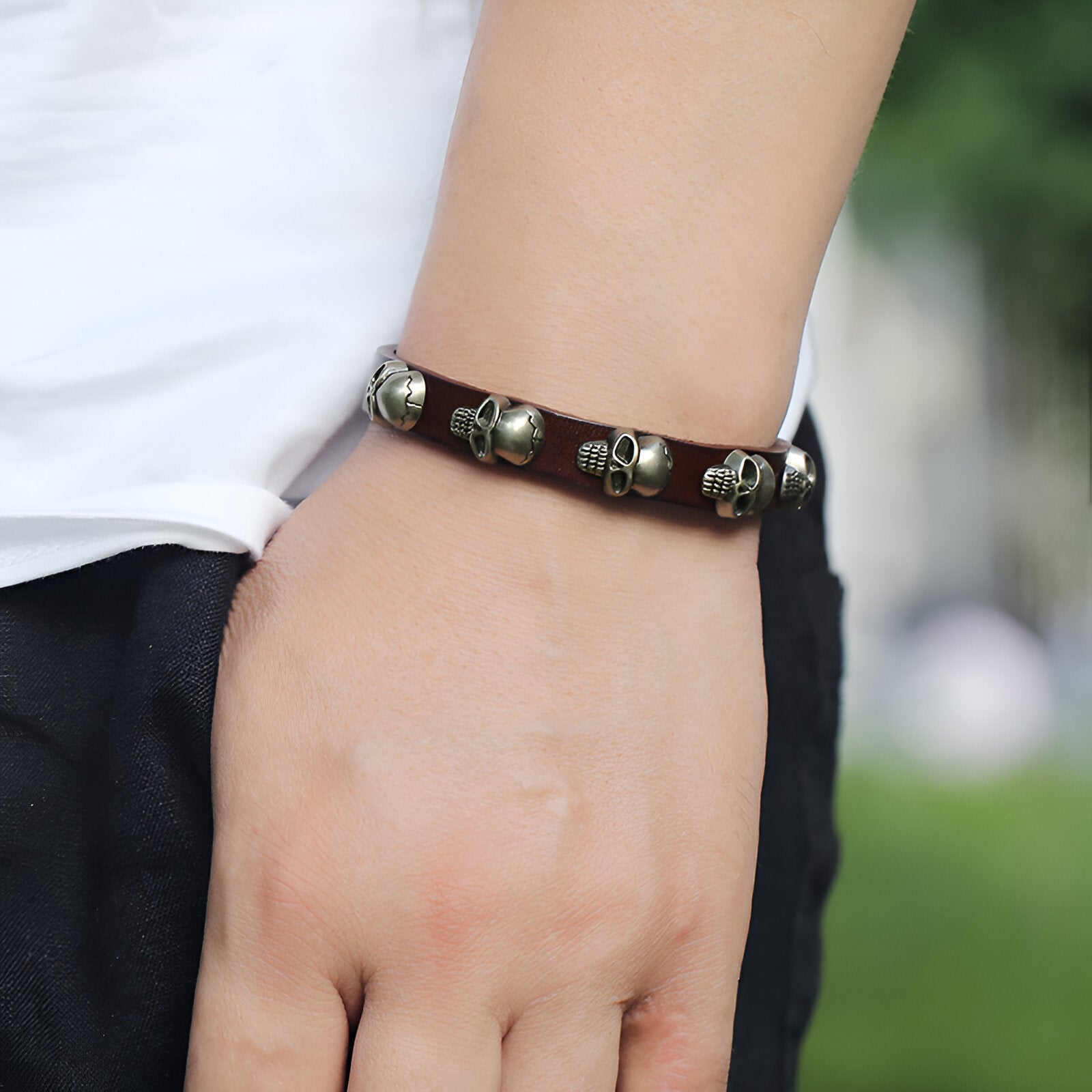 Bracelet en cuir marron avec plusieurs têtes de mort en métal gris porté au poignet homme.