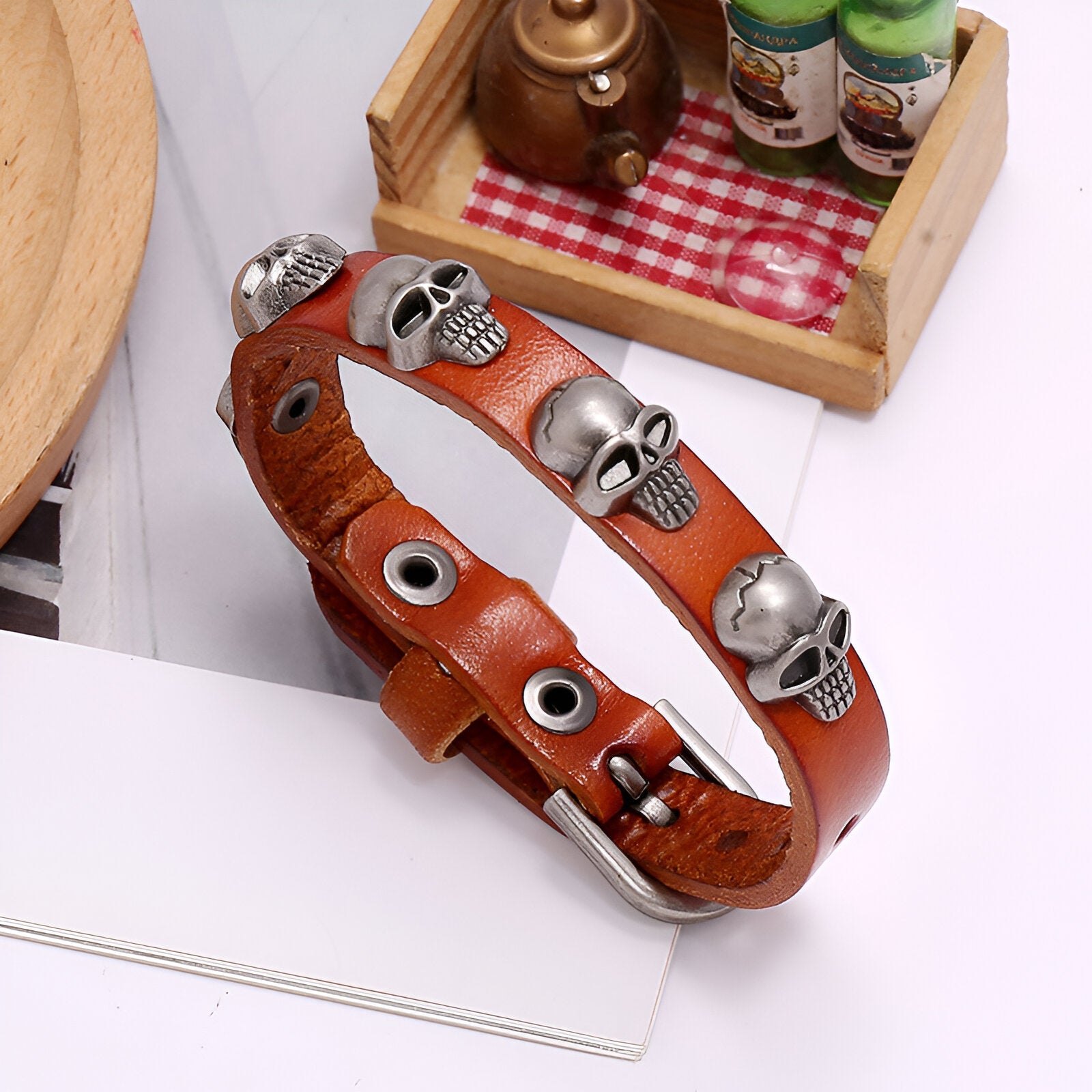 Bracelet en cuir café avec têtes de mort en métal argenté et rivets noirs.