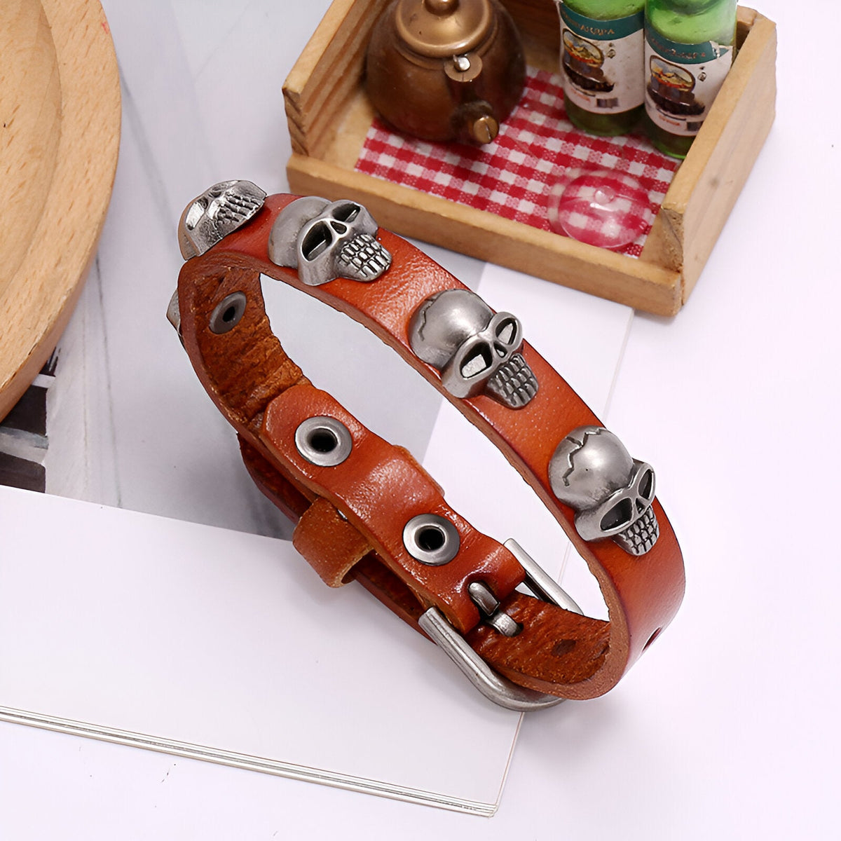 Bracelet en cuir café avec têtes de mort en métal argenté et rivets noirs.