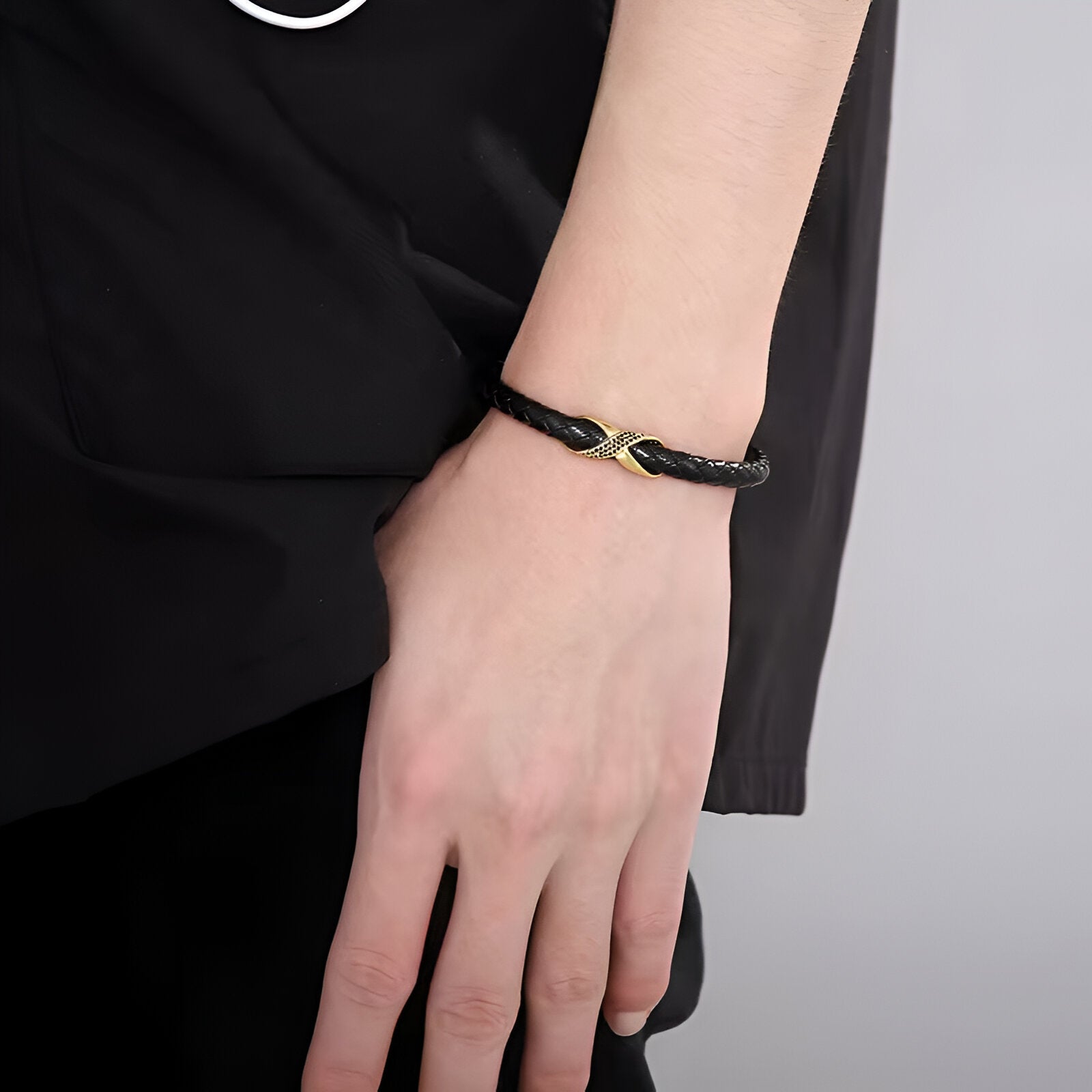 Bracelet en cuir noir tressé avec nœud central en acier doré sur poignet masculin.