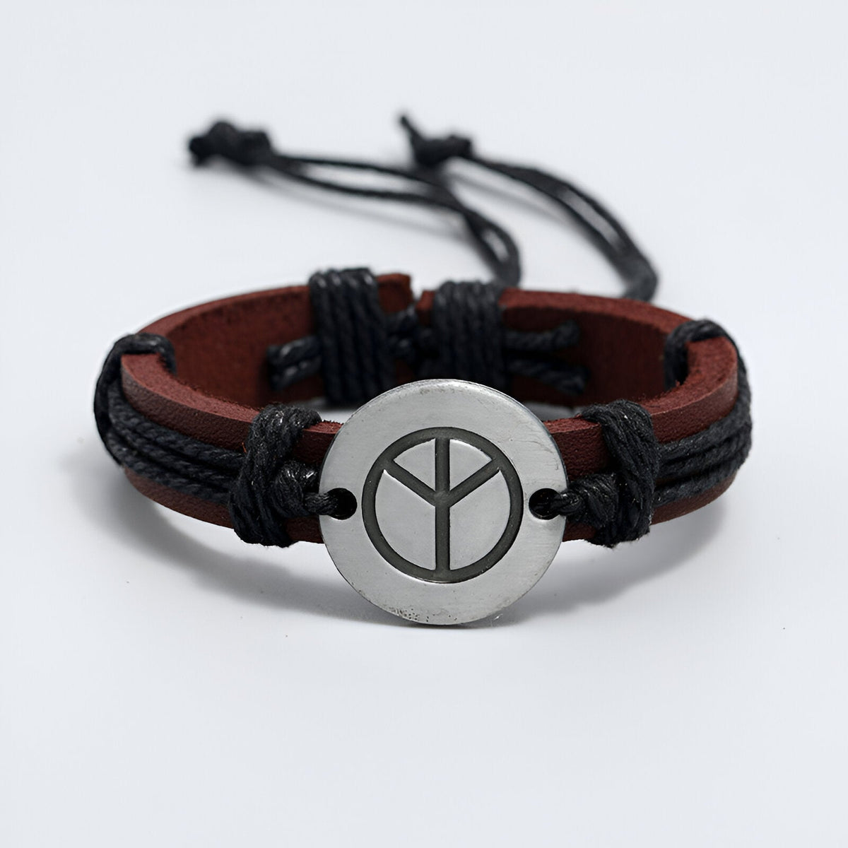 Bracelet en cuir marron à double lanière avec pendentif rond en métal argenté arborant un symbole de paix noir.