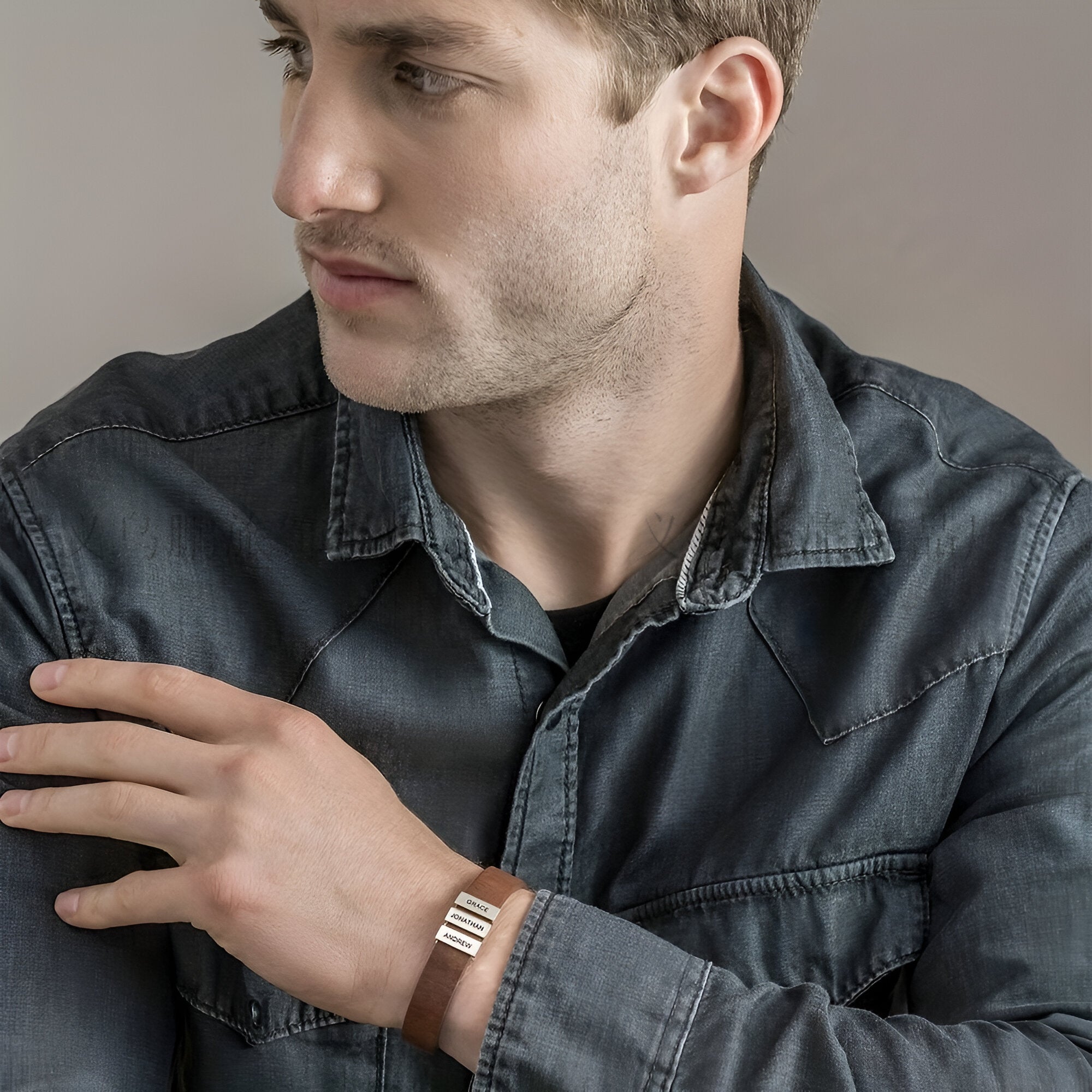 Bracelet en cuir marron avec deux plaques métalliques gravées porté par un homme en chemise sombre.