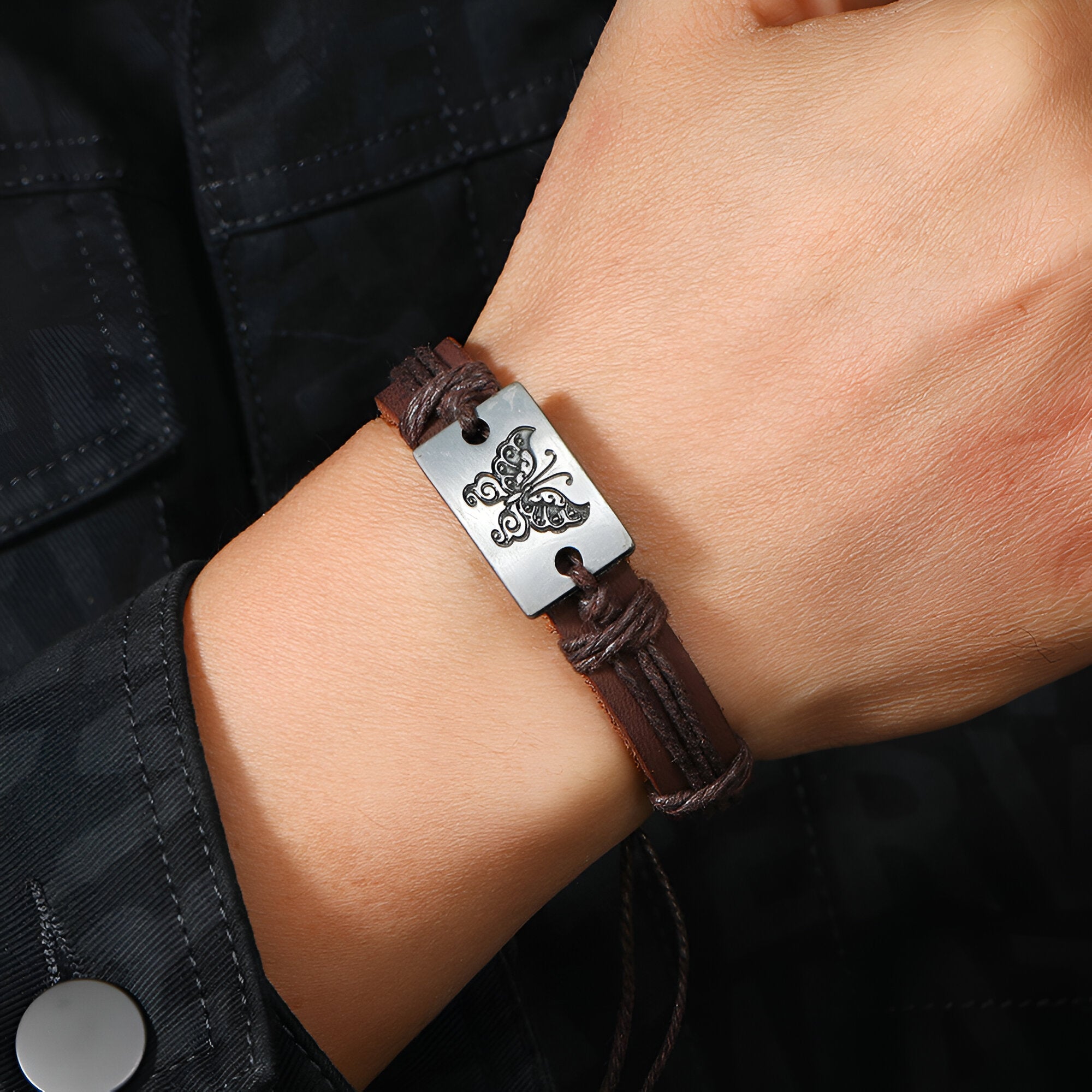 Bracelet en cuir café avec plaque métallique argentée gravée d’un motif papillon.