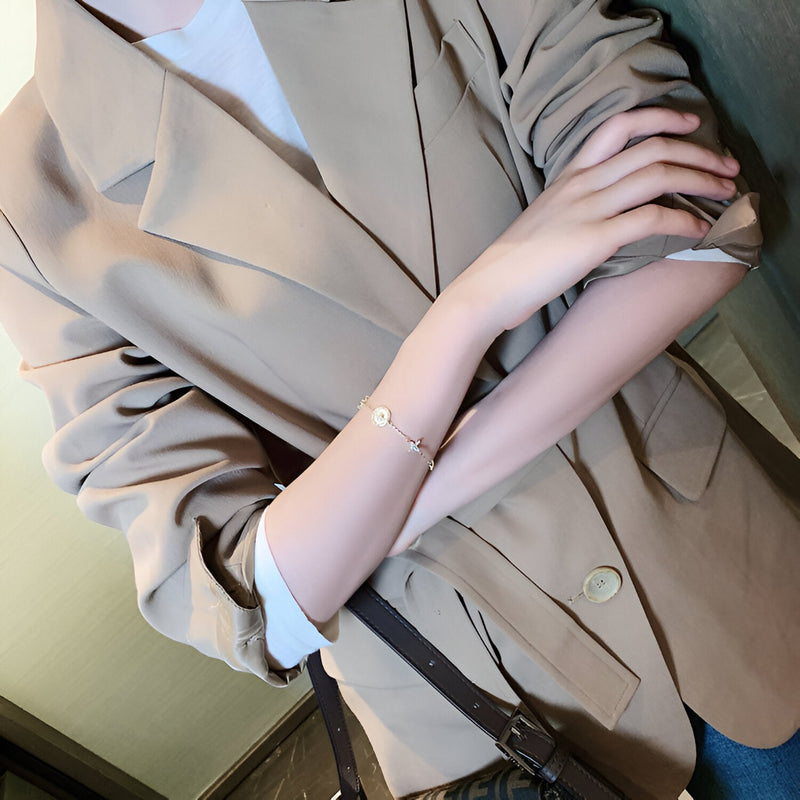 Bracelet fin en cuivre plaqué or avec pendentif trèfle à 4 feuilles porté au poignet féminin.