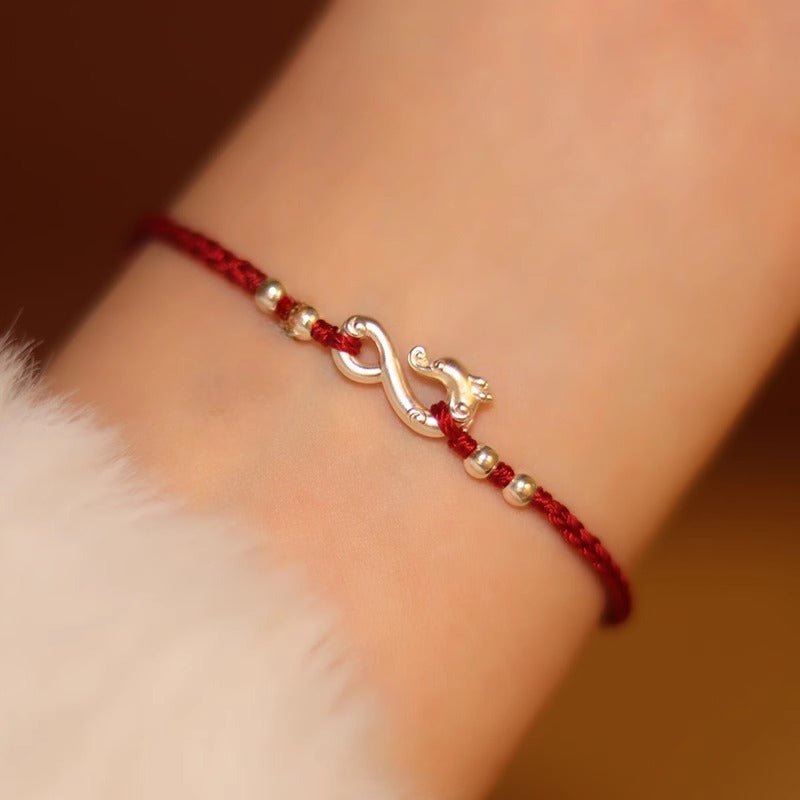 Bracelet en fil rouge ciré avec pendentif infini et dragon en métal doré, style fin et élégant.