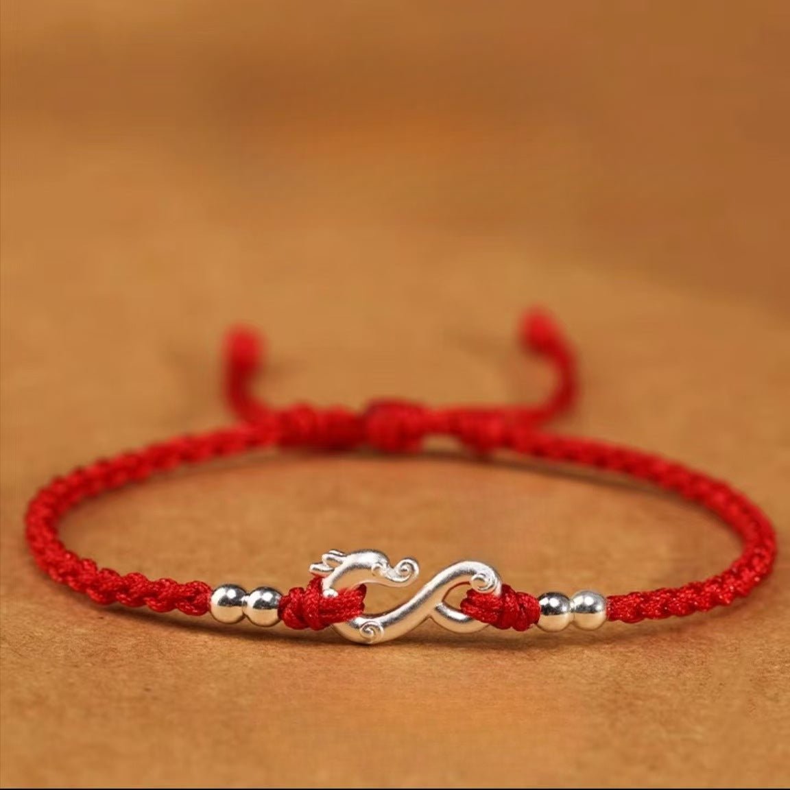 Bracelet rouge en fil ciré avec symbole infini et détails en métal argenté, style tressé.