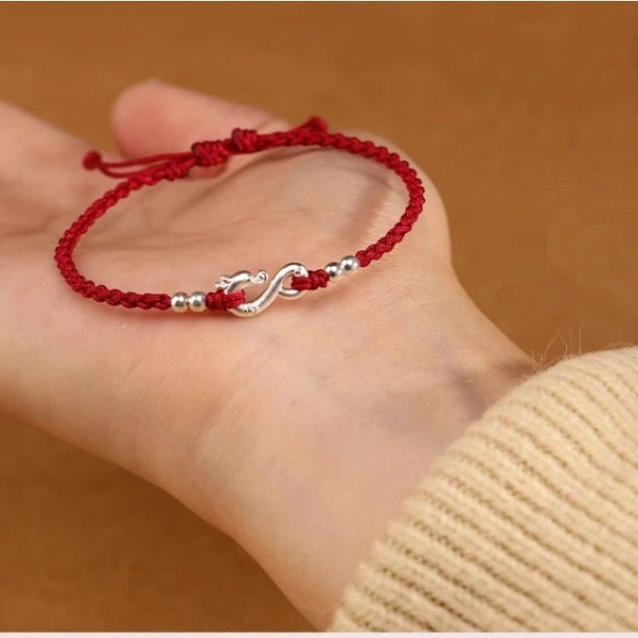 Bracelet en fil rouge ciré avec symbole infini en métal argenté, porté au poignet, style minimaliste.
