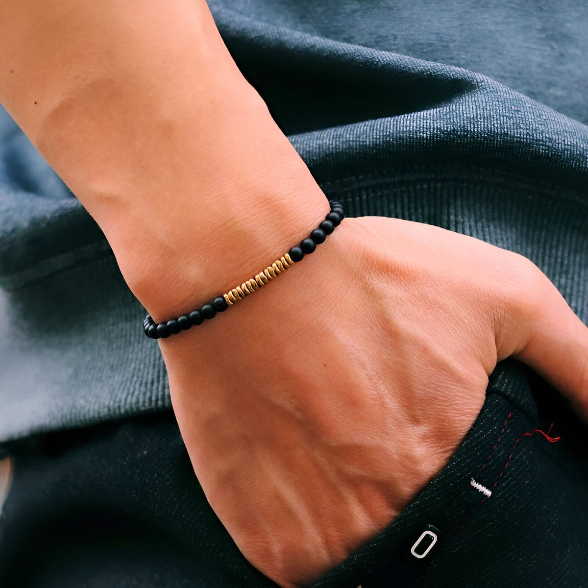 Bracelet fin pour homme en hématite noire avec perles dorées cylindriques.