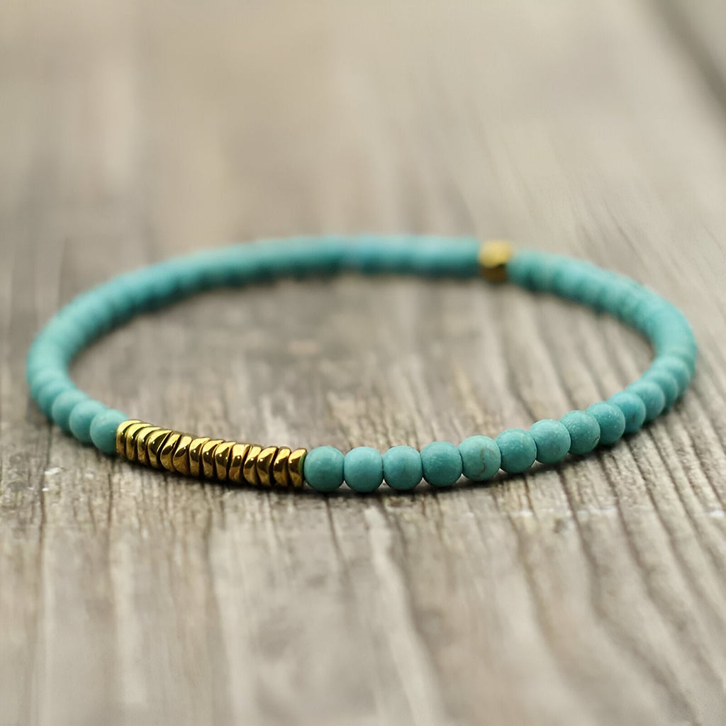 Bracelet fin en perles turquoise avec accents en hématite dorée sur corde élastique.
