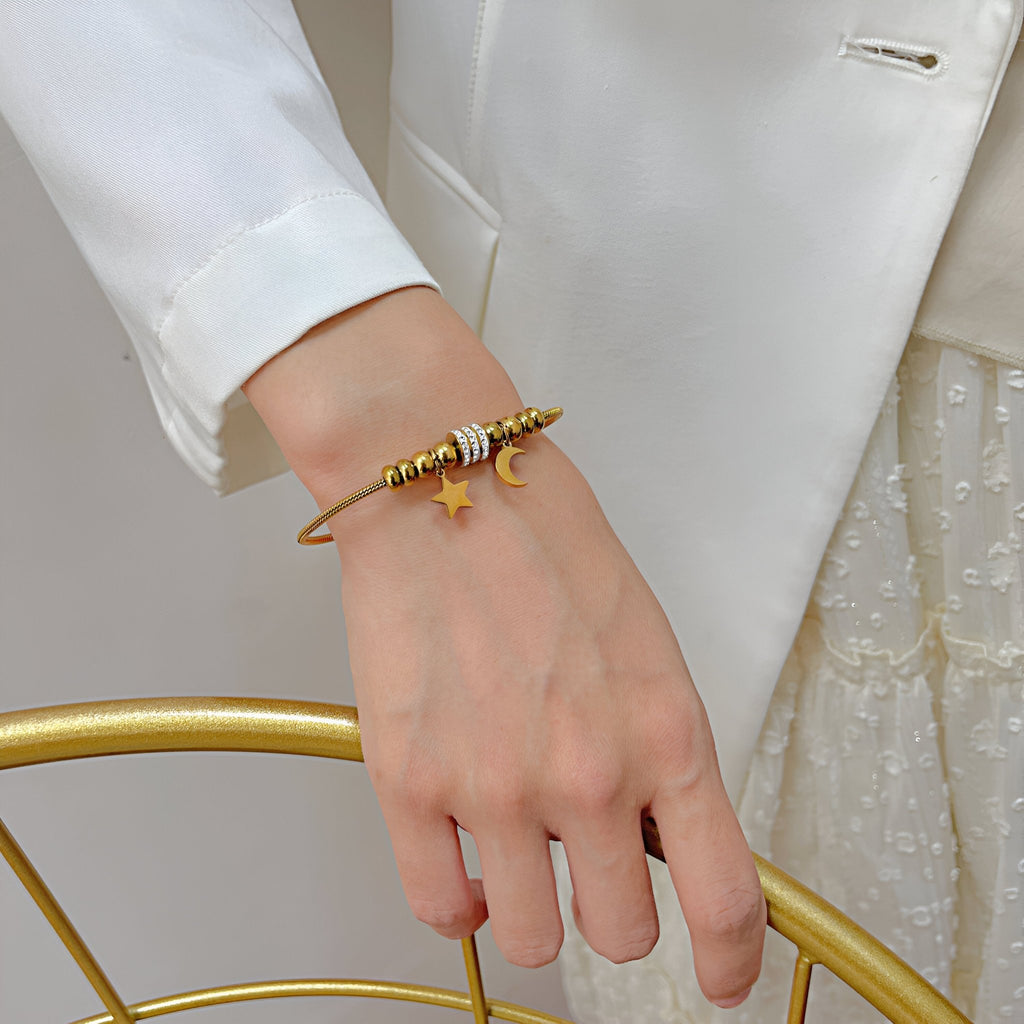 Bracelet serpent fin en acier inoxydable doré avec pendentifs lune et étoile scintillants.