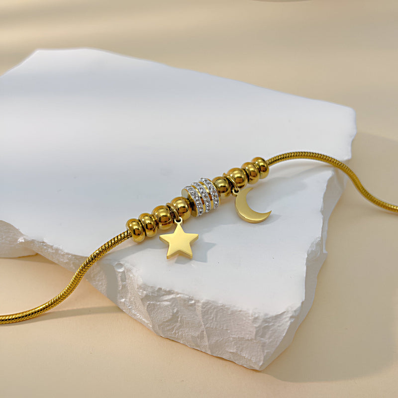 Bracelet maille serpent doré avec pendentifs lune, étoile et perles strassées en acier inoxydable.