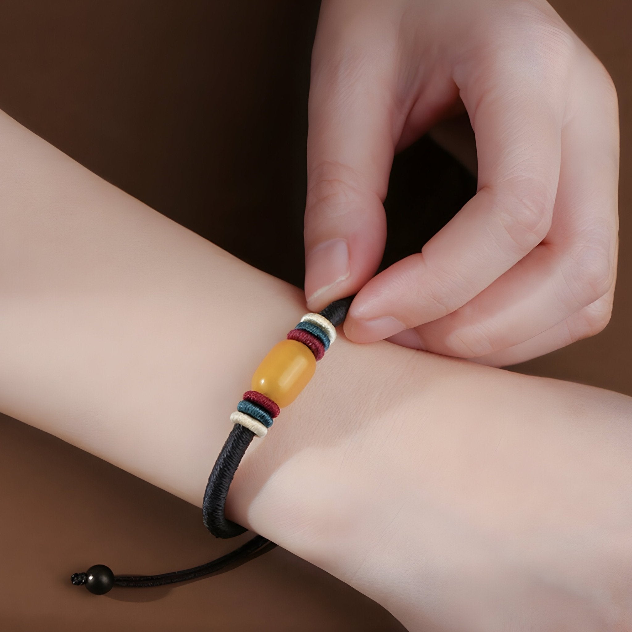 Bracelet mixte en nylon noir avec perle centrale en pierre d'ambre jaune et détails colorés.