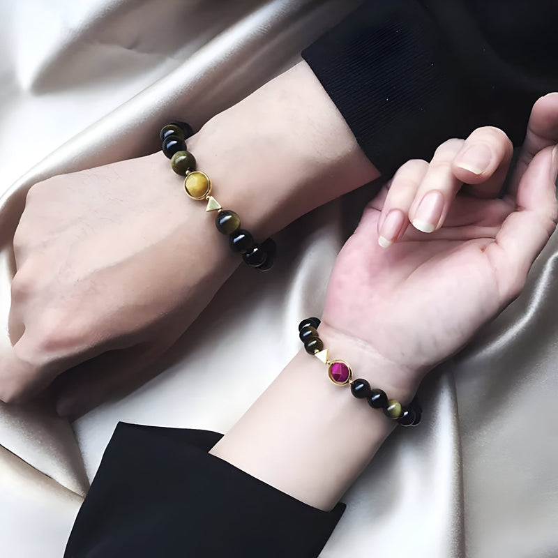 Bracelets en perles noires d'obsidienne avec perles centrales en oeil de tigre jaune et rose sur poignets croisées, style.