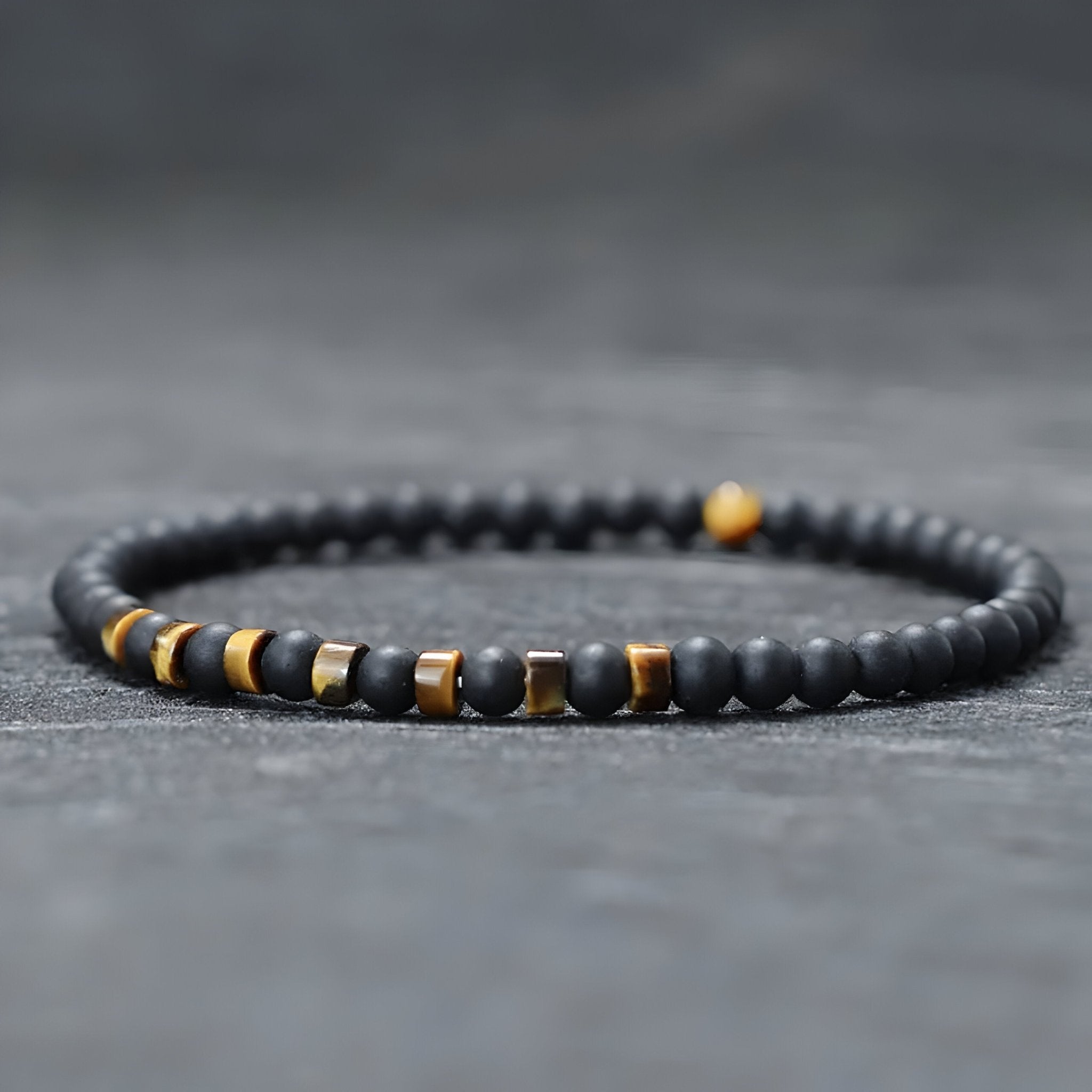 Bracelet fin pour homme en perles noires d'onyx avec accents métalliques et pierres jaunes œil de tigre.