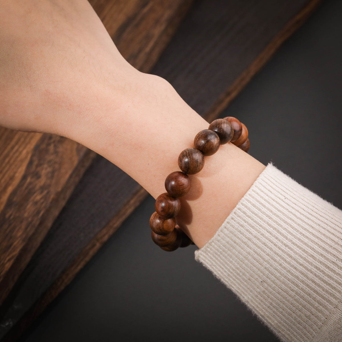 Bracelet Shelia en perles rondes bois de rose marron foncé portée sur poignet avec manche beige côtelé.