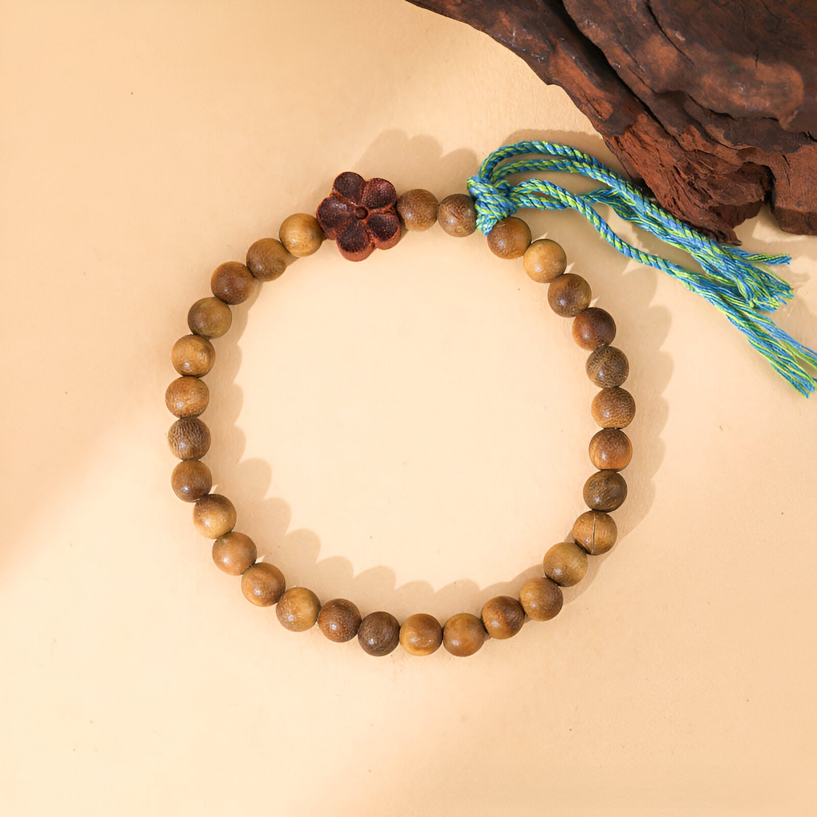 Bracelet en perles rondes marron en bois de santal avec ornement floral et pompon turquoise.