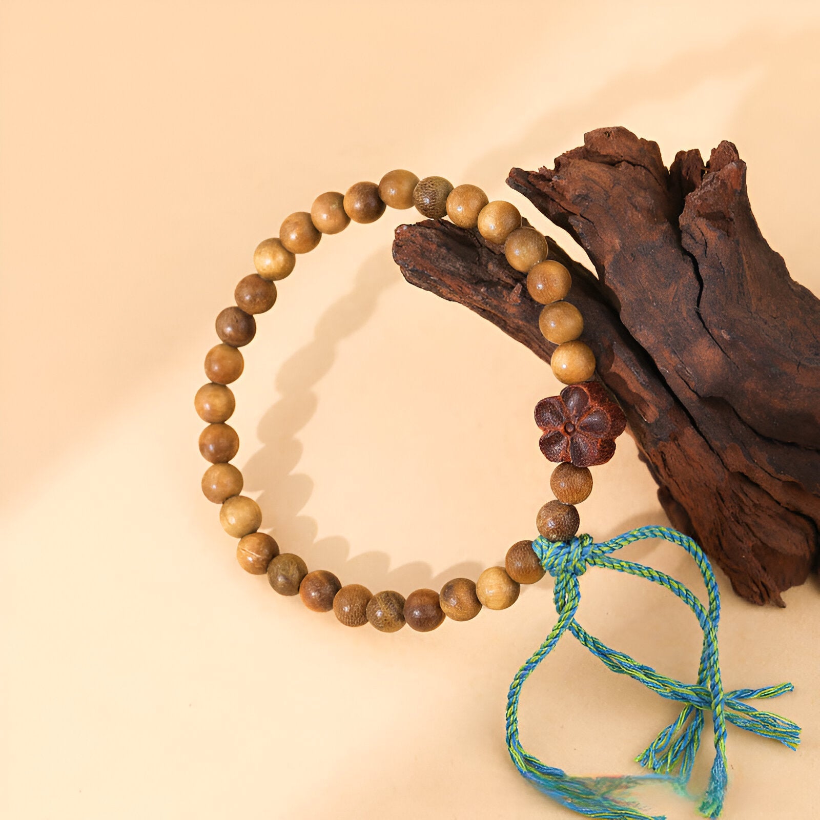Bracelet en perles de bois de santal marron avec ornement floral et cordon turquoise noué.