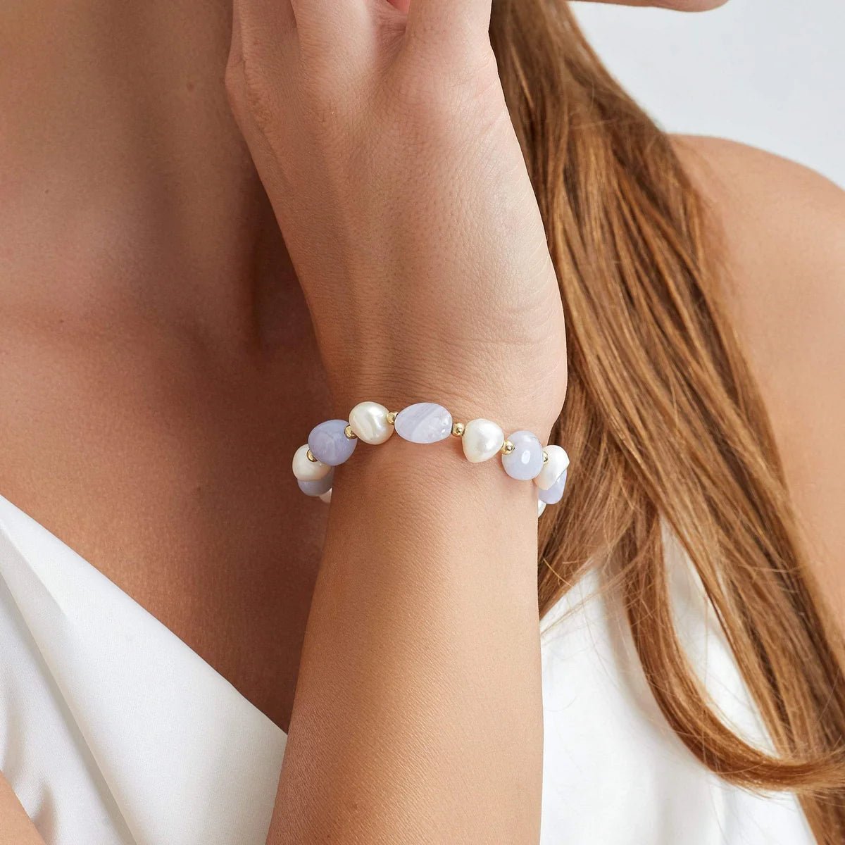 Bracelet ajustable perles d'eau douce blanches avec petits anneaux dorés sur poignet féminin.