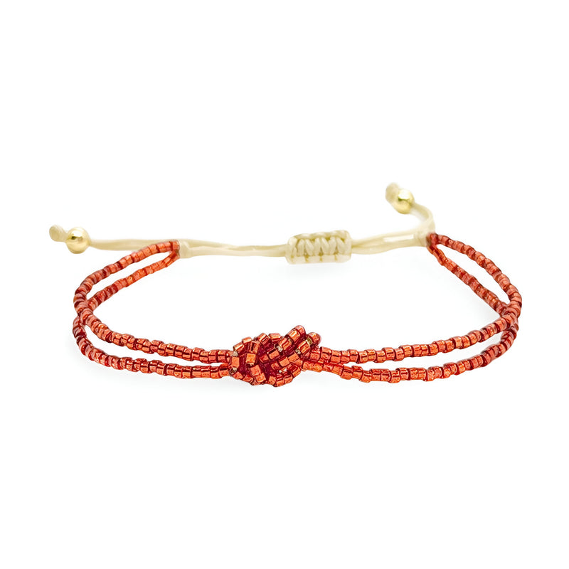 Bracelet femme perles rouges du Japon avec nœud central et cordon beige ajustable.