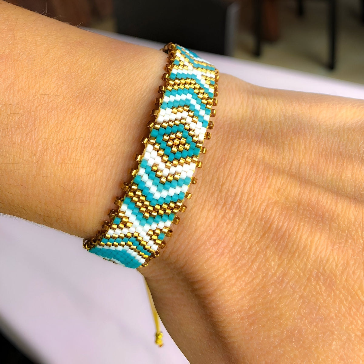 Bracelet ajustable en perles japonaises bleues, blanches et dorées avec motif géométrique arrondi.