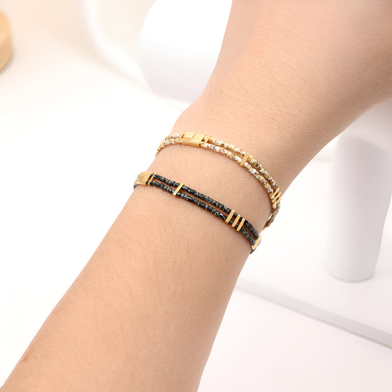 Bracelet double-rangs ajustable en perles japonaises, un rang beige clair et un rang noir avec détails dorés.