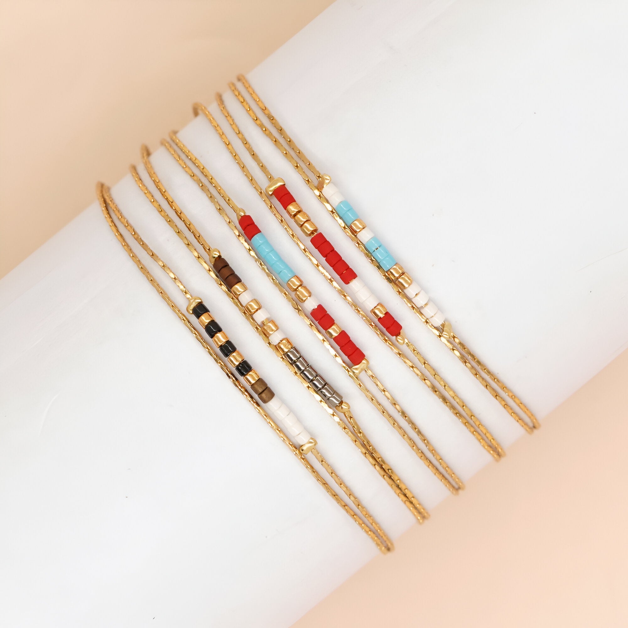 Bracelets double-rangs en perles rouges, bleues, noires, blanches et grises avec chaîne dorée fine.