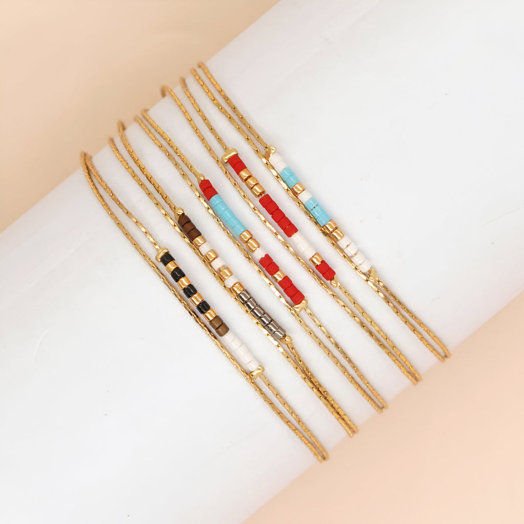 Bracelets double-rangs en perles rouges, bleues, noires, blanches et grises avec chaîne dorée fine.