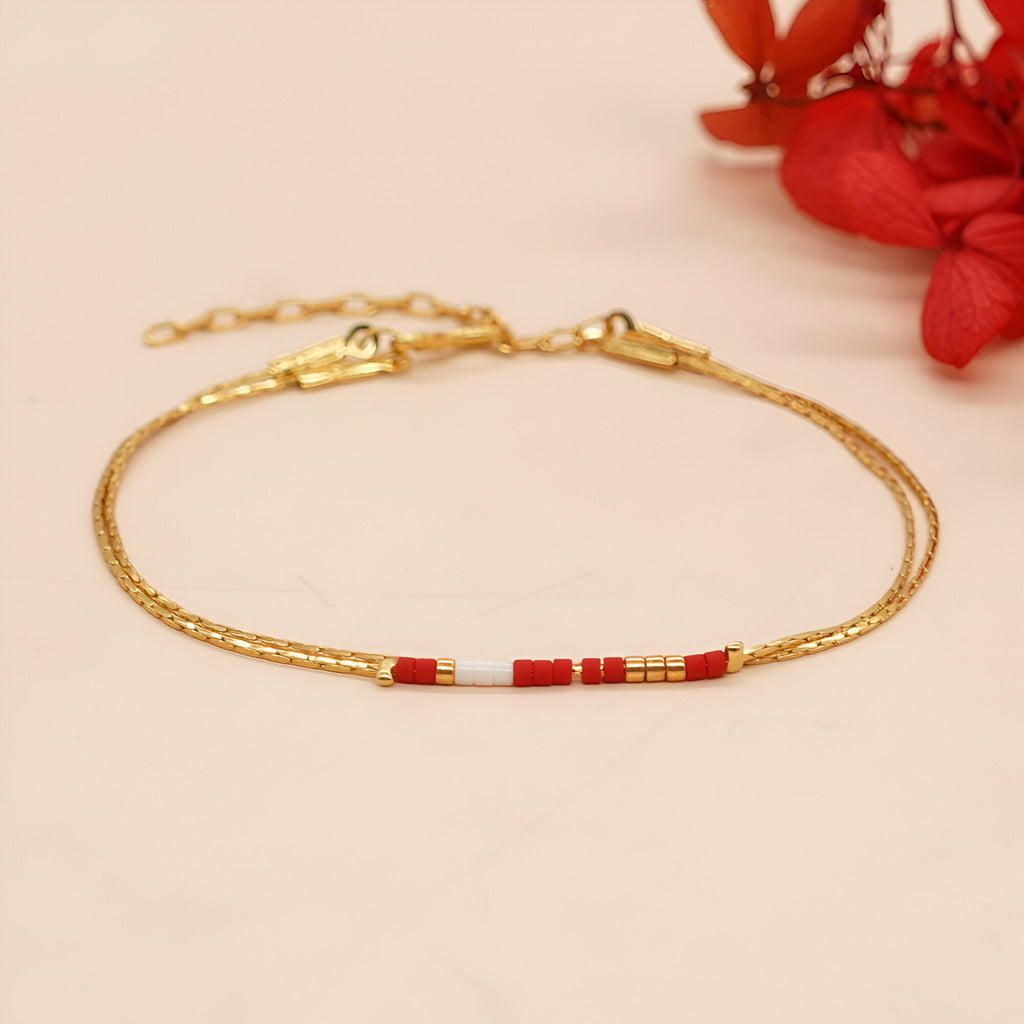 Bracelet fin double-rangs en perles rouges et blanches avec chaînette dorée et fermoir lobster.