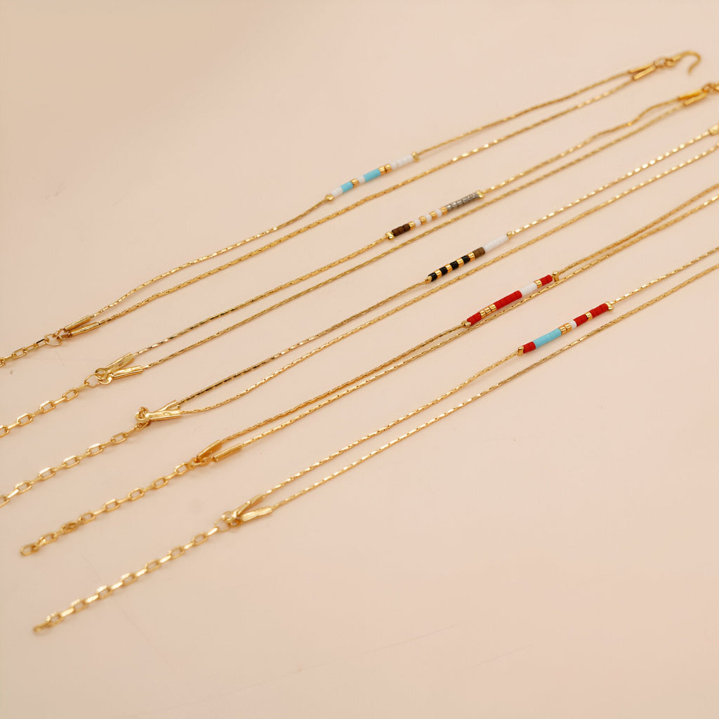 Bracelet double-rangs en perles rouges, bleues et blanches avec chaînes fines dorées.