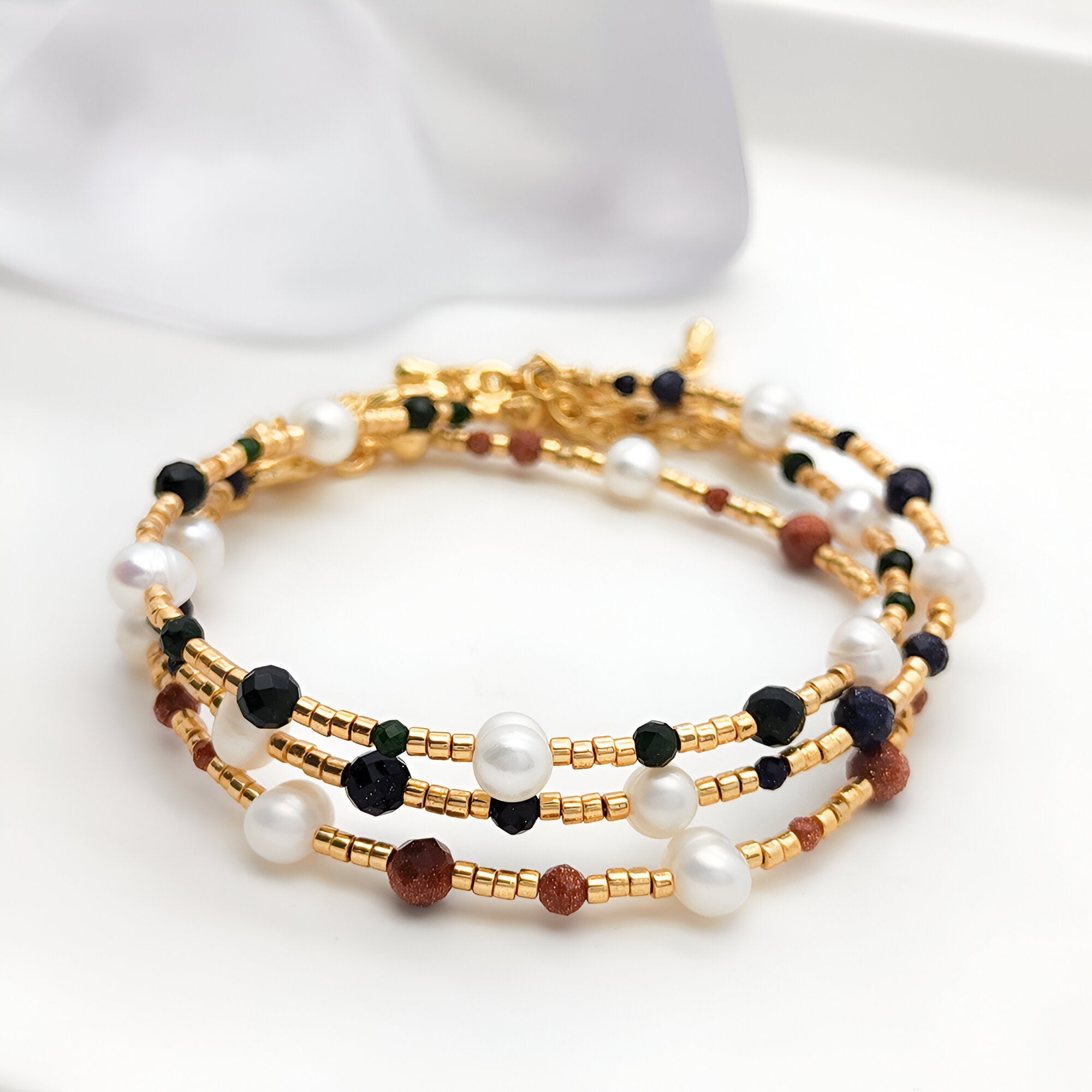 Bracelet femme multi-rangs en perles dorées, pierres de grès marron, perles noires et blanches élégantes.