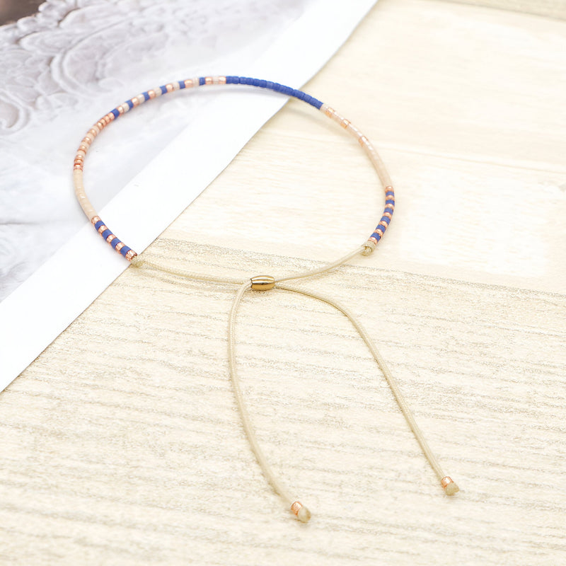 Bracelet fin en perles bleues, blanches et dorées, fermoir coulissant doré élégant.