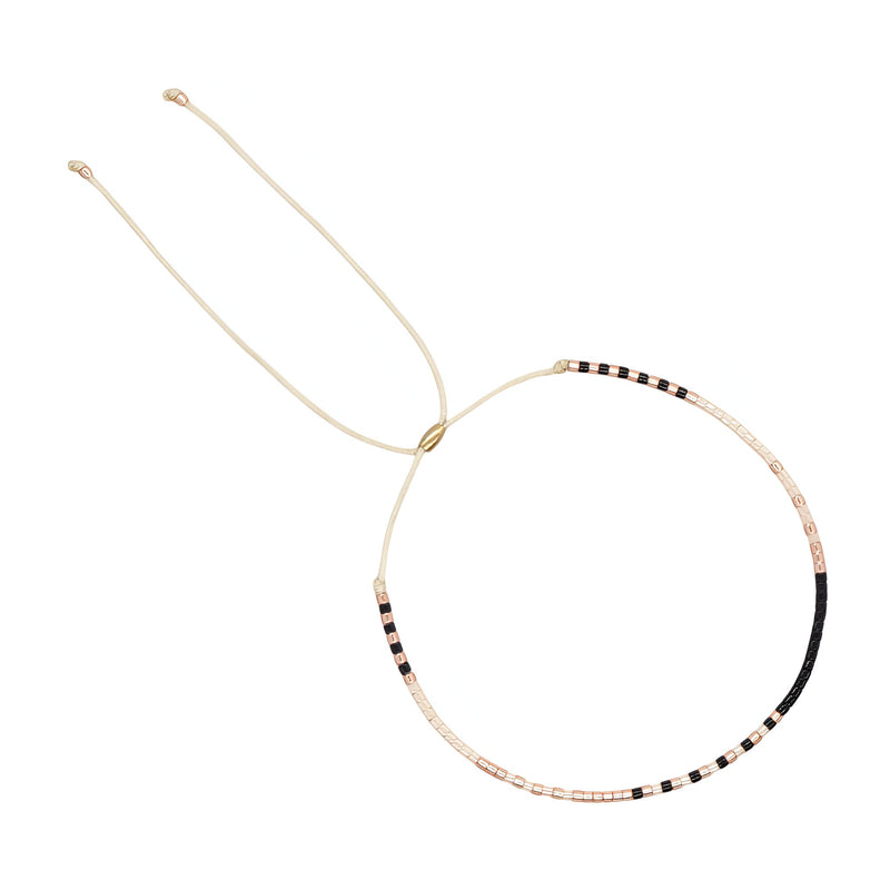 Bracelet fin à perles noires, beiges et blanches, réglable avec cordon beige léger.