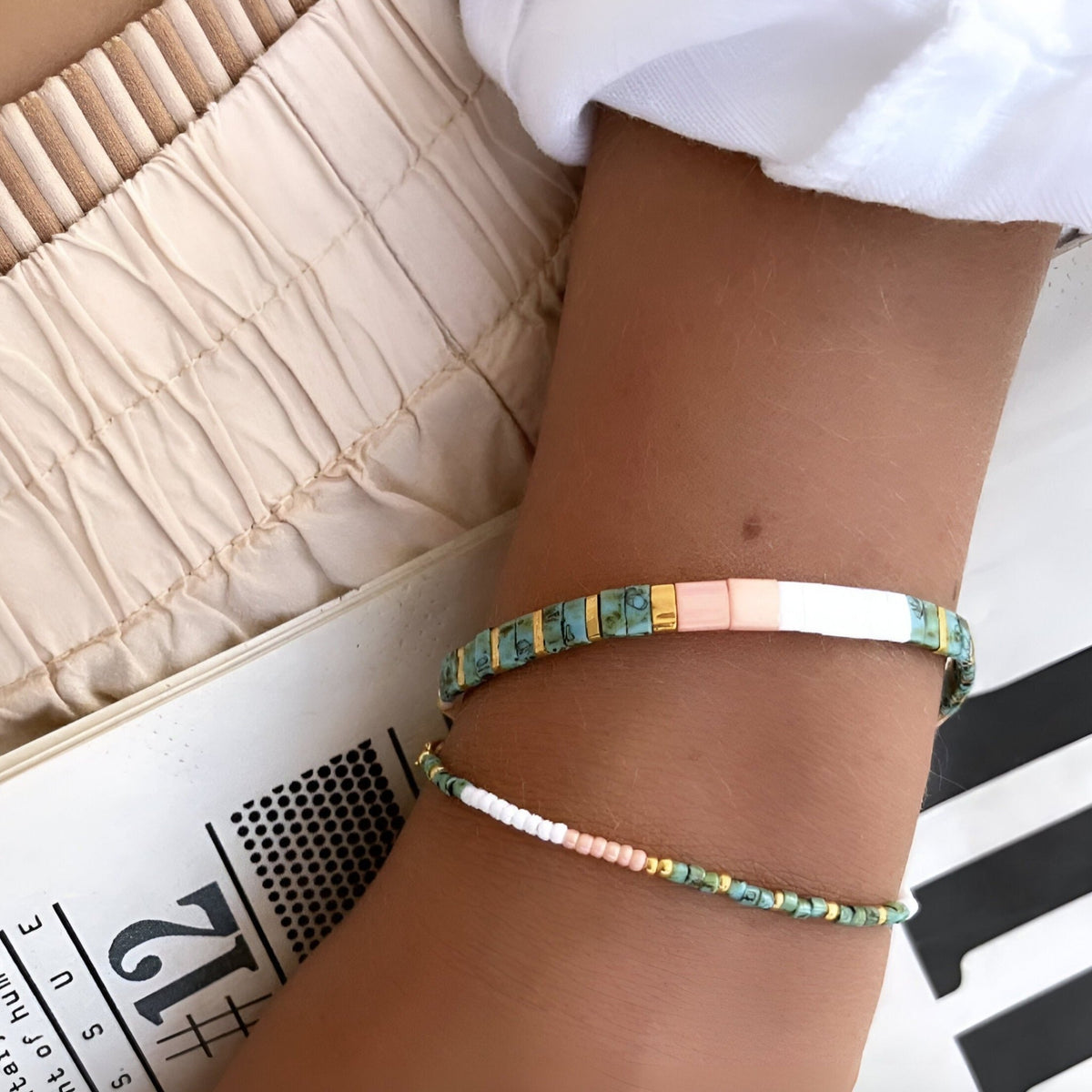 Bracelet double tour perles bleu, vert, rose et blanc avec détails dorés sur poignet féminin.
