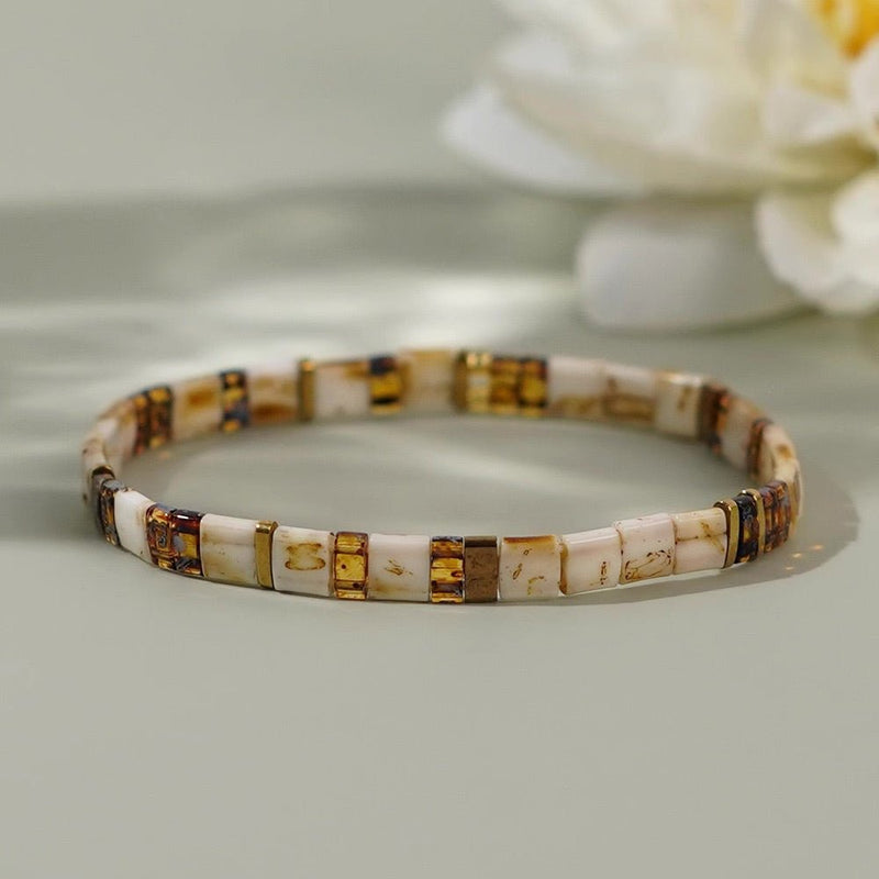 Bracelet marron en perles japonaises rectangulaires avec motifs dorés et blanc cassé.