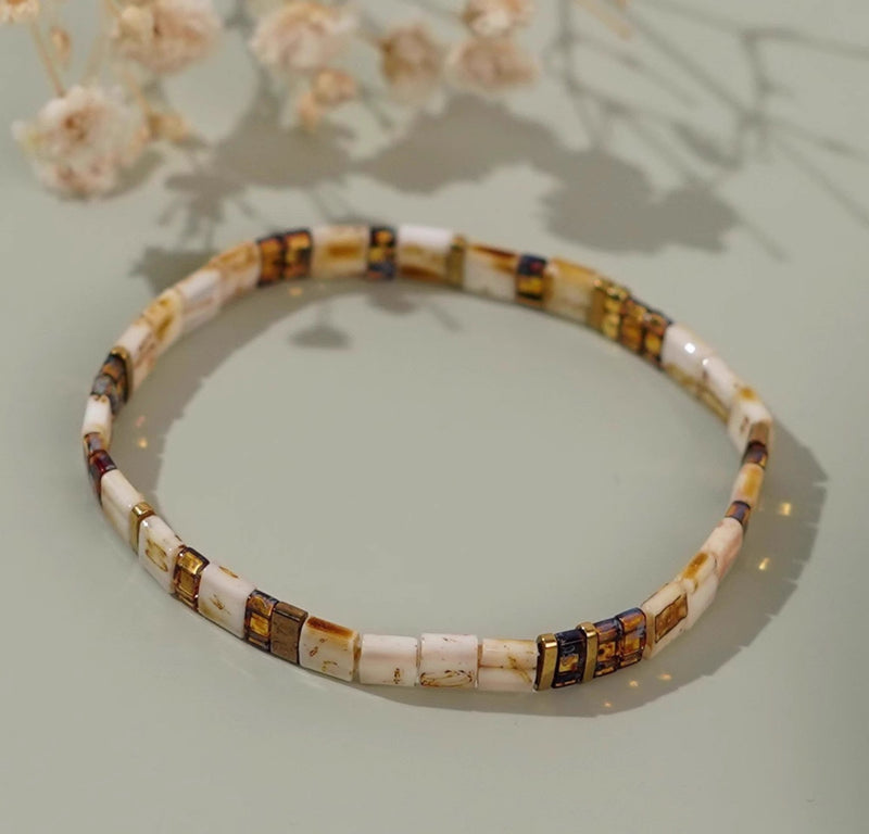 Bracelet fin en perles marron et ivoire avec détails bleu marine, style minimaliste élégant.