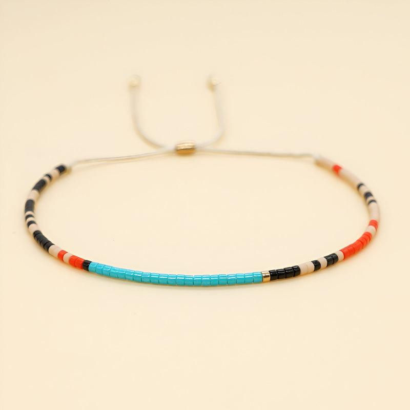 Bracelet fin en perles japonaises multicolores bleu, noir, blanc et rouge sur fil ajustable beige.