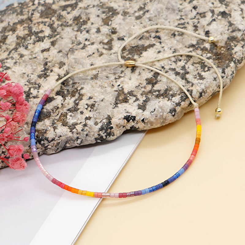 Bracelet en perles fines multicolores style Kumiko, fermeture ajustable dorée, posé sur pierre texturée.