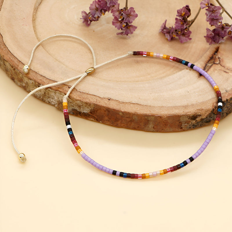 Bracelet fin en perles japonaises multicolores style Kumiko avec cordon beige réglable sur fond bois clair.