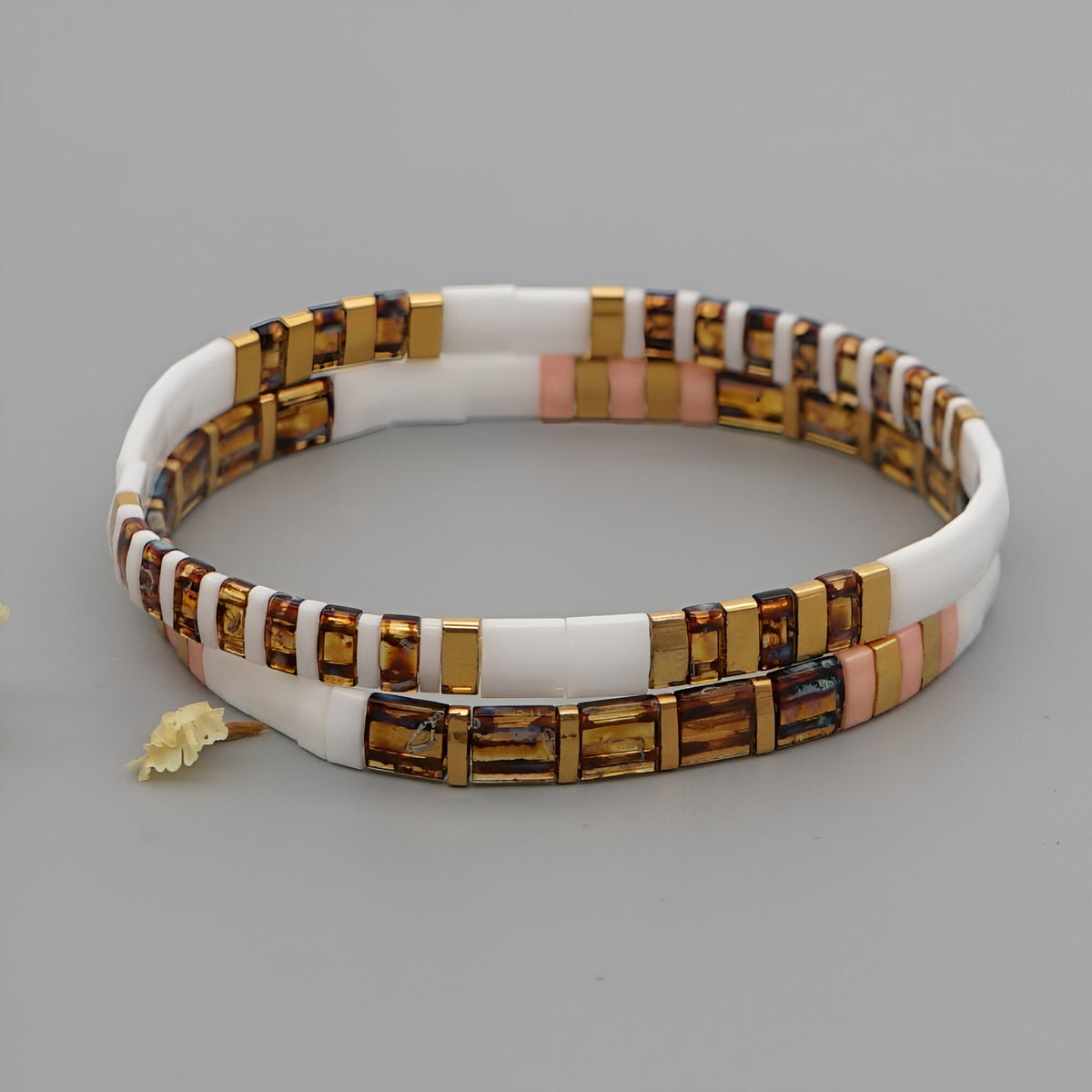 Bracelet double tour pour femme en perles plates blanches, mates et dorées avec petites touches roses et breloque feuille.