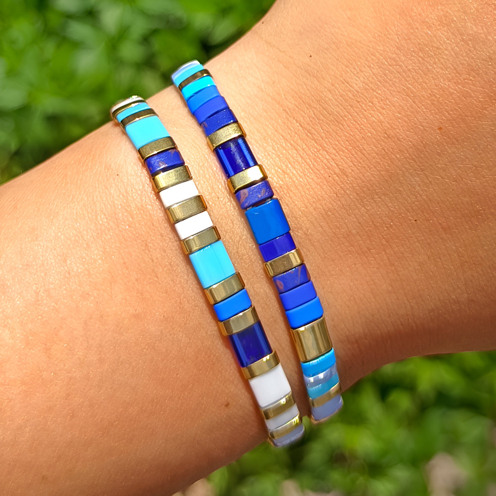 Deux bracelets en perles carrées bleu, turquoise, blanc et or, style Okawo, portés au poignet.