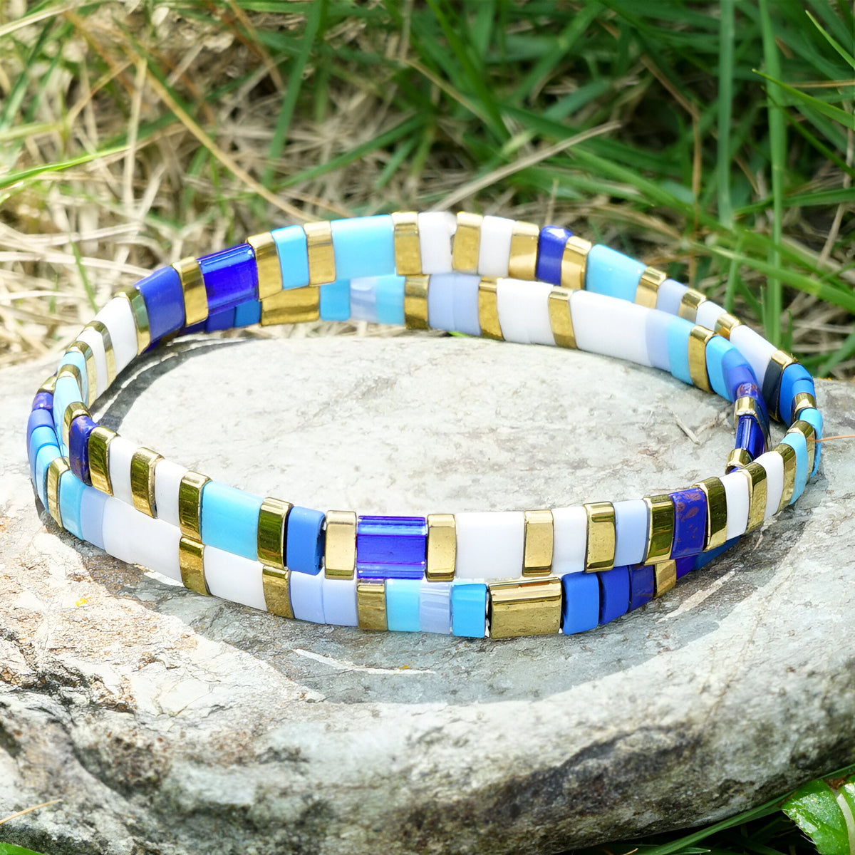 Bracelet double tour en perles japonaises bleues, blanches, dorées et turquoise posé sur pierre en extérieur.