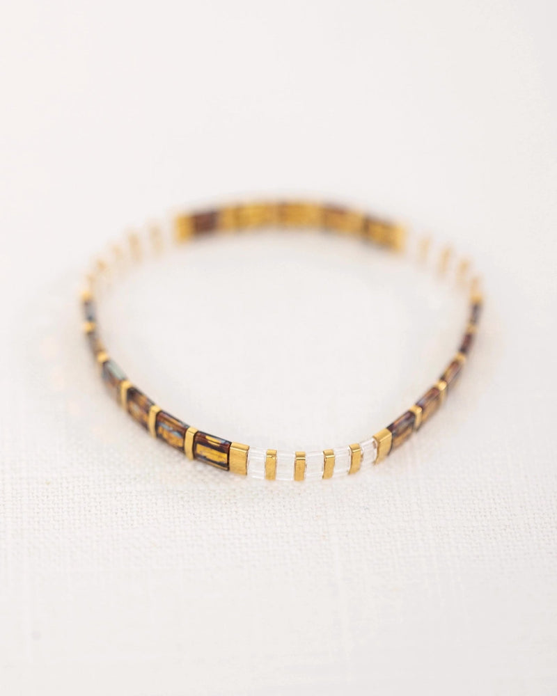 Bracelet fin marron avec perles japonaises alternant sections dorées et transparentes.