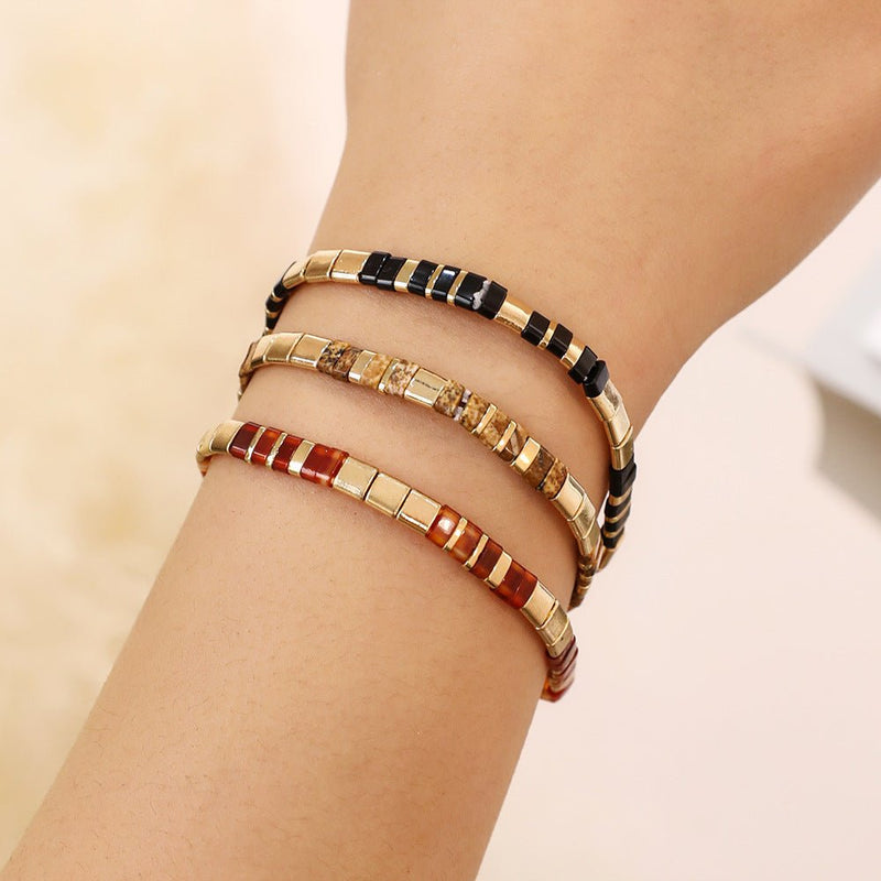 Bracelet souple à enfiler en perles japonaises multicolores rouges, noires et dorées avec accents brillants.